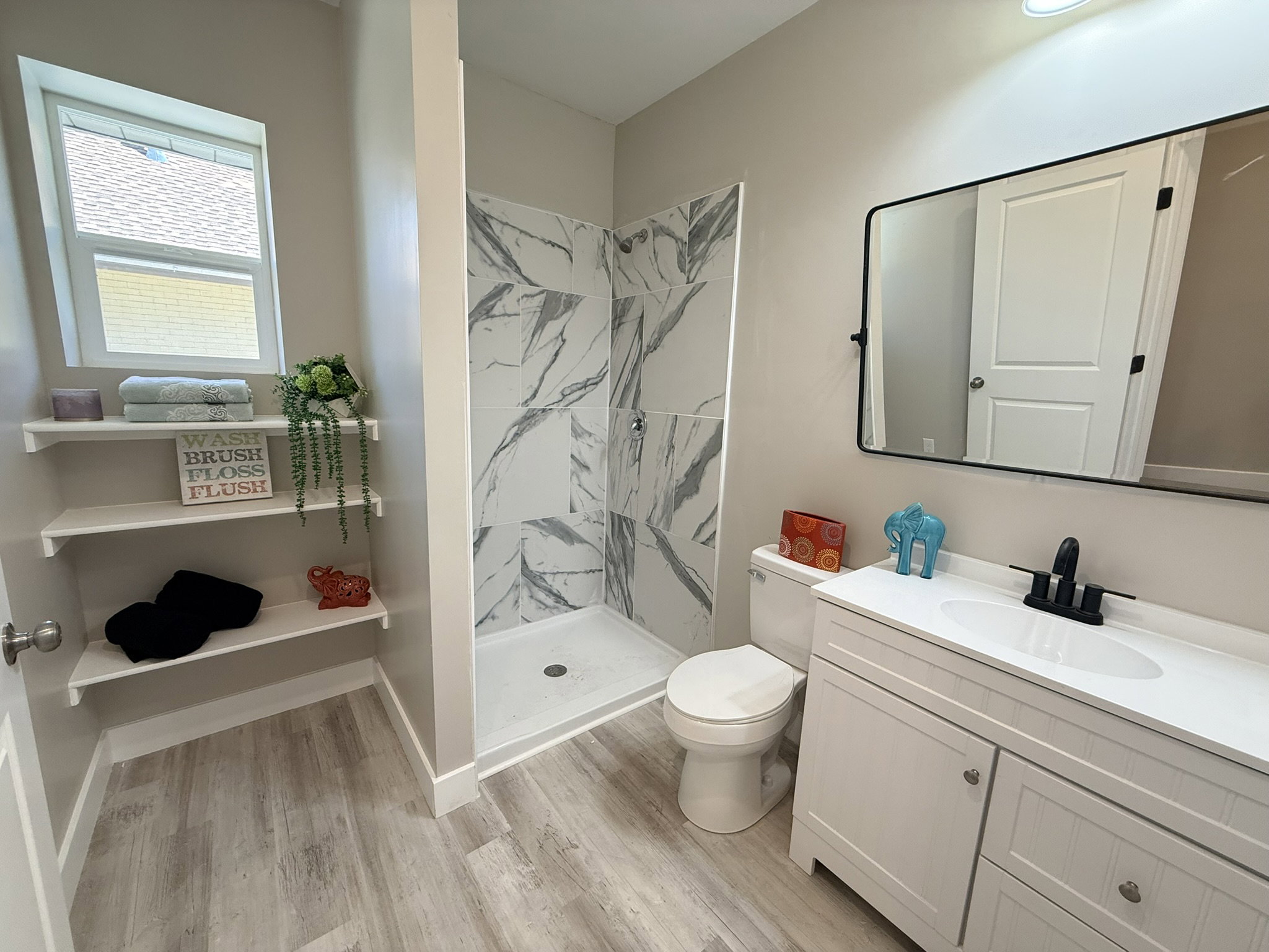 Bathroom featuring a walk-in shower with marble-look tile, a white vanity with integrated sink, and wood-finish flooring