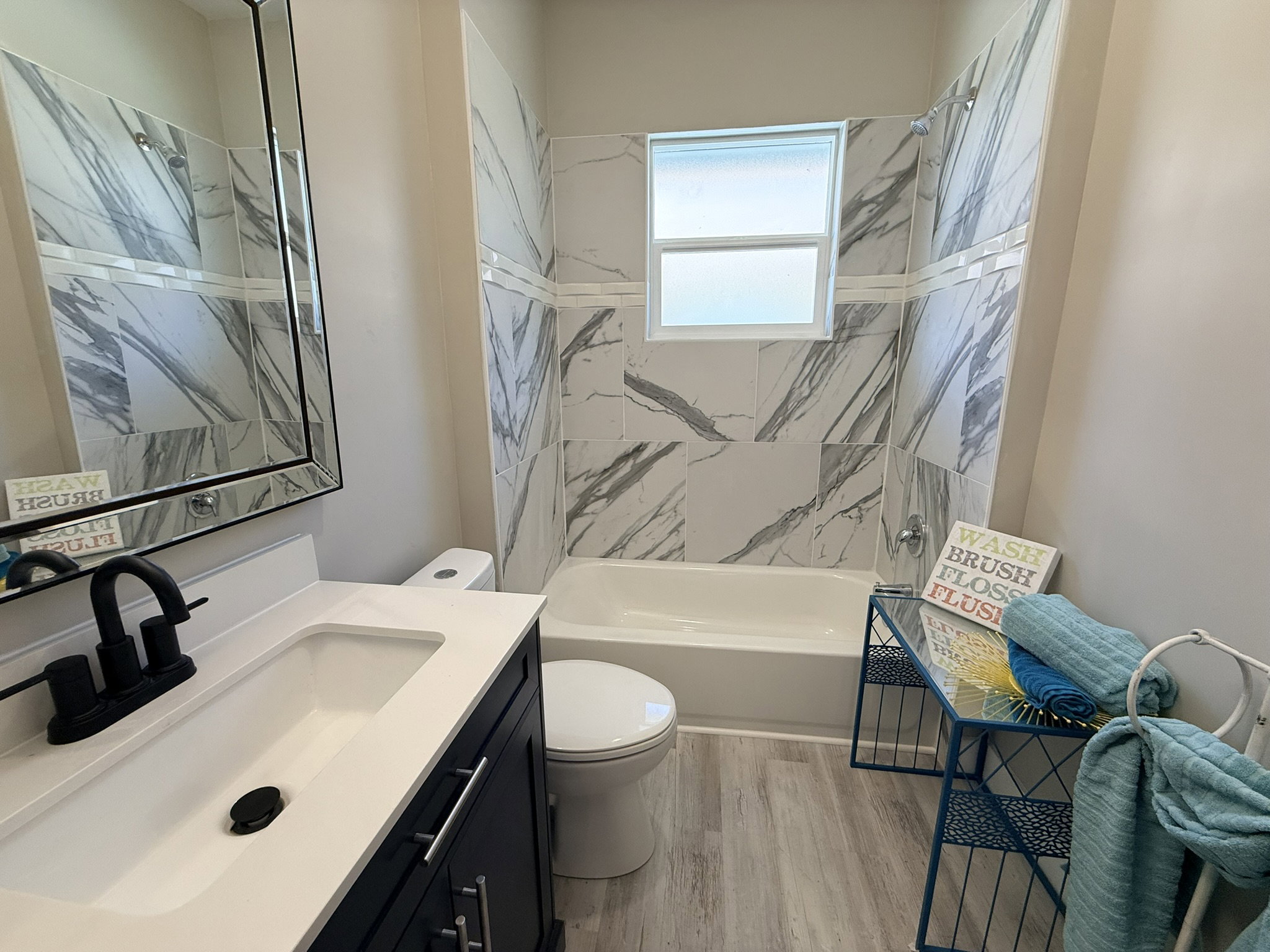 Full bathroom featuring a single vanity with a white countertop, matte black faucet, and a large framed mirror