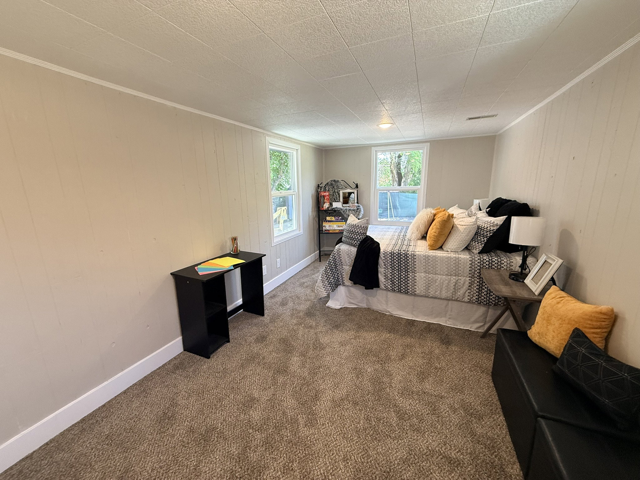 Carpeted room featuring two windows, vertical paneled walls, white baseboards, and a textured ceiling