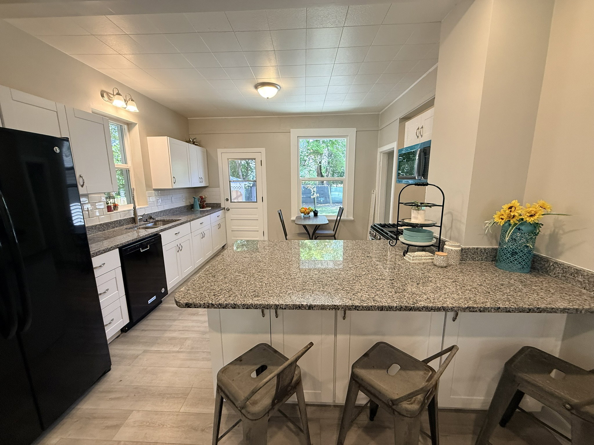 Kitchen featuring an extended island with a stone countertop, white cabinetry, a tile backsplash, and light wood-finish flooring
