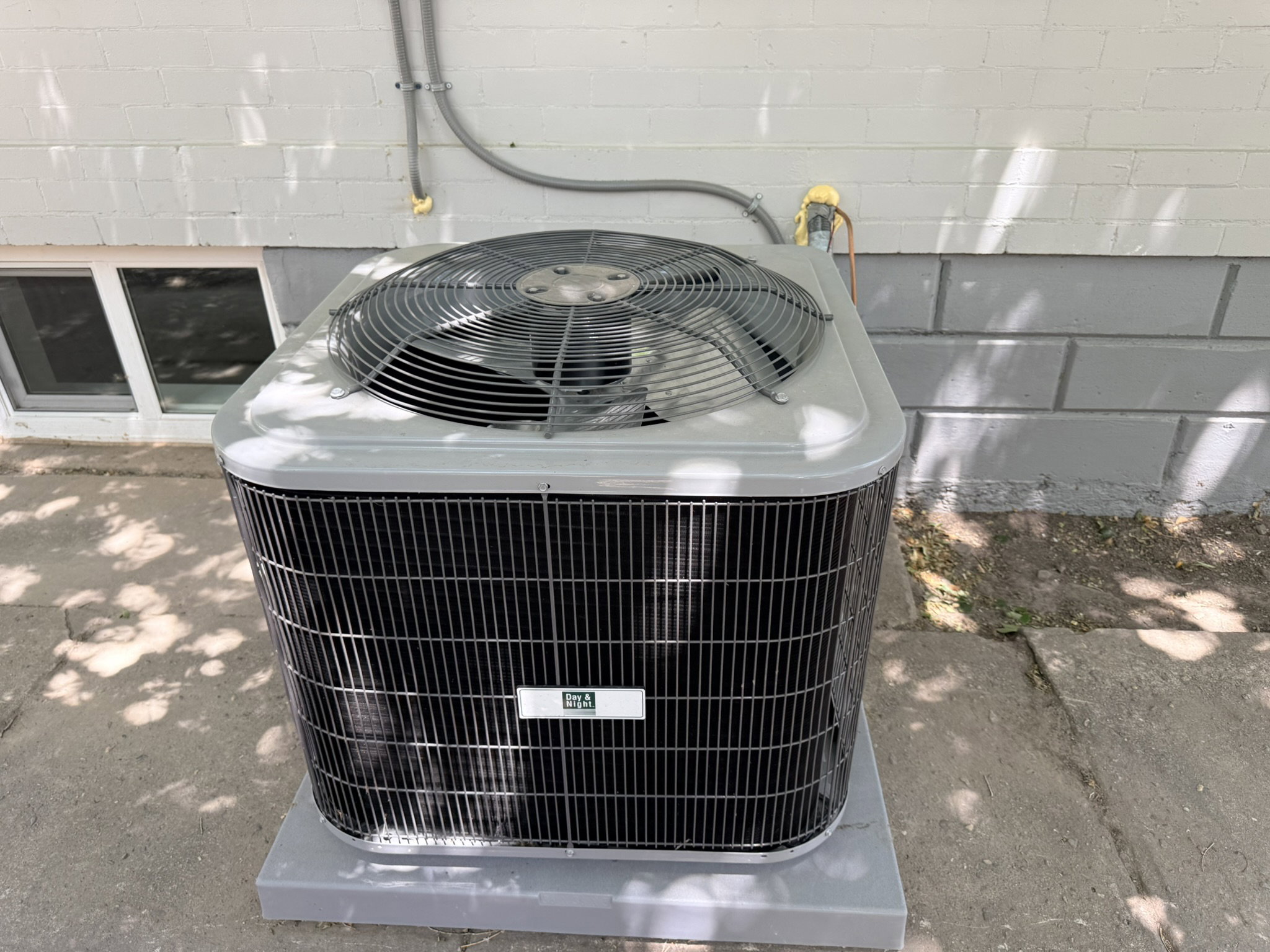 Central air conditioning unit on a concrete pad, set against a painted concrete block wall