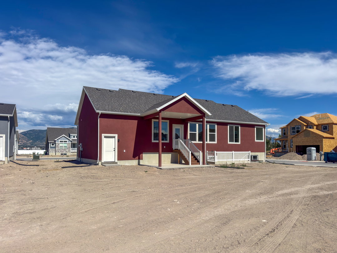 Newly constructed residence featuring a deep red exterior with white trim, a covered patio, and a walk-out basement entry