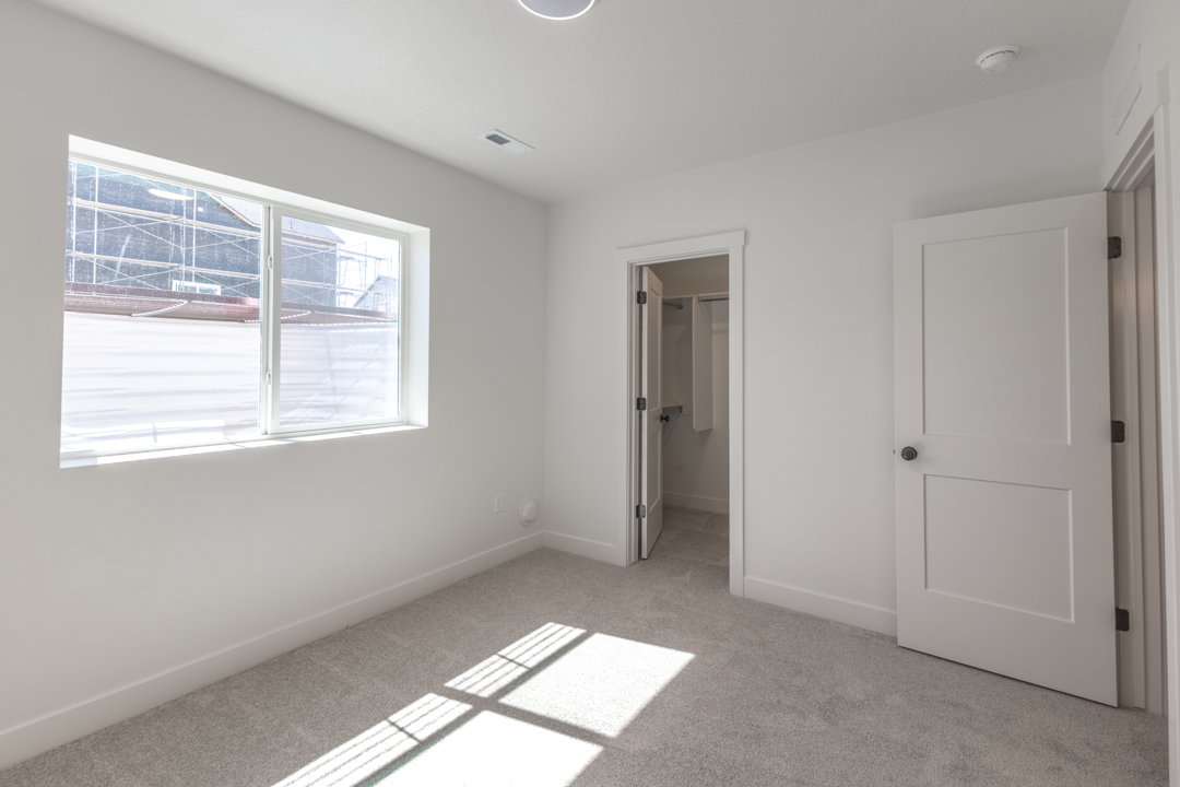 Carpeted room with a large window, a ceiling light fixture, a door with a black knob, and a separate closet with a bifold door