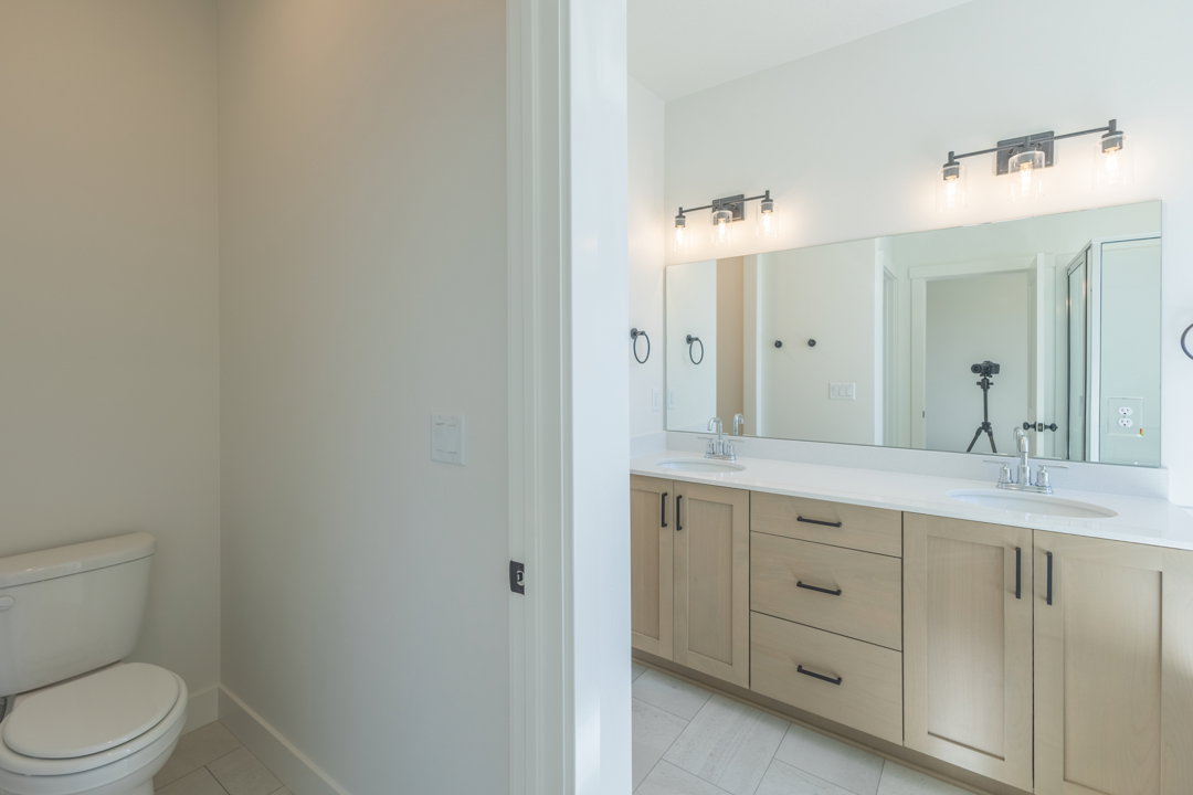Bathroom featuring a dual vanity with light-toned cabinetry, white countertops, and contemporary black hardware