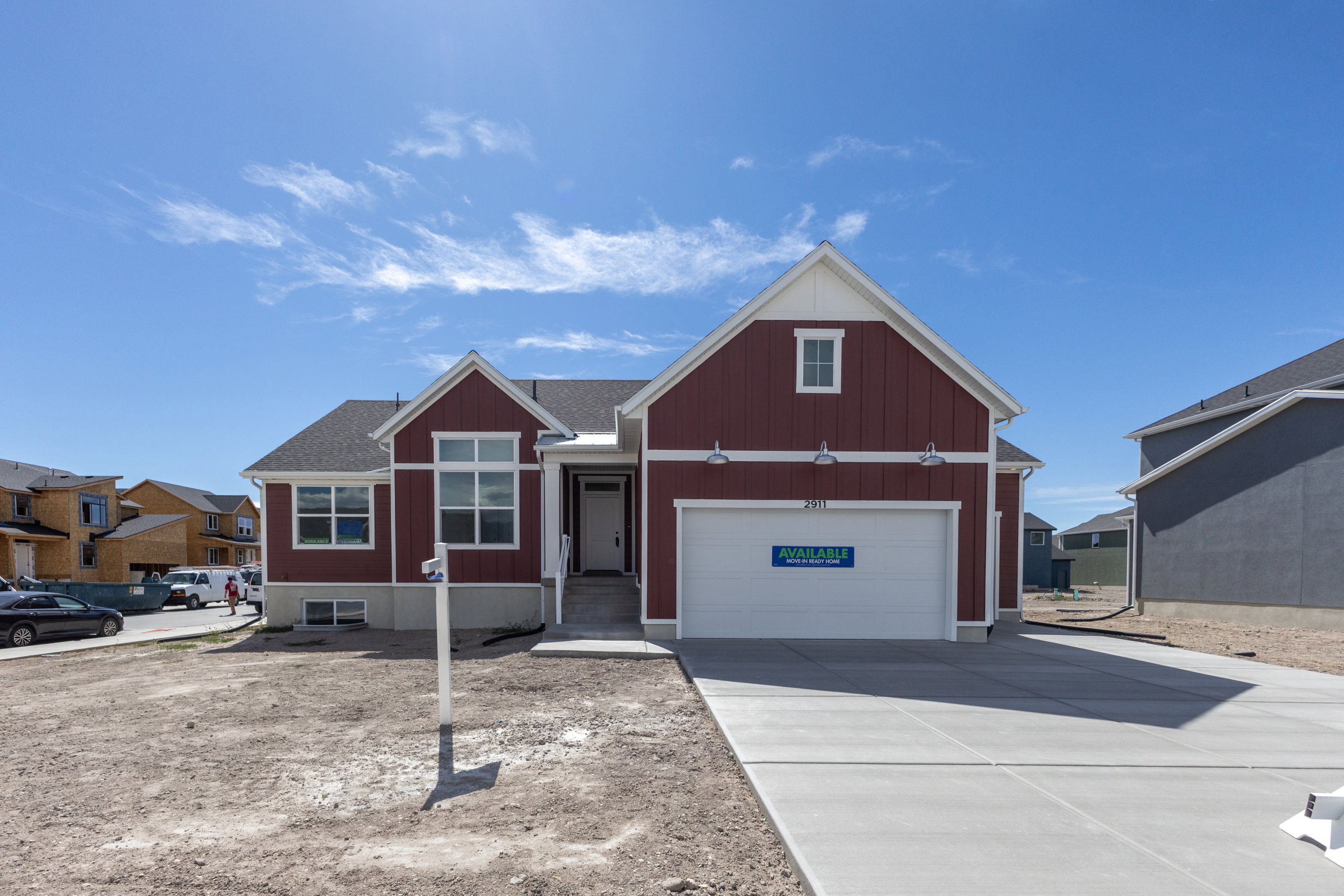 Single-story residence featuring a two-car garage, red vertical siding, white trim accents, and a dark shingle roof