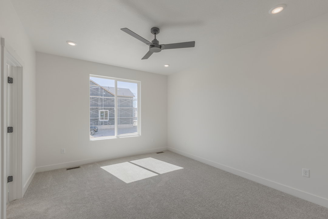 Bright room with a large window, light gray carpet, and a modern ceiling fan