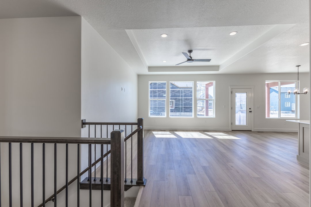 Spacious open-concept living area featuring wood-finish flooring, a tray ceiling with recessed lighting, and a modern ceiling fan