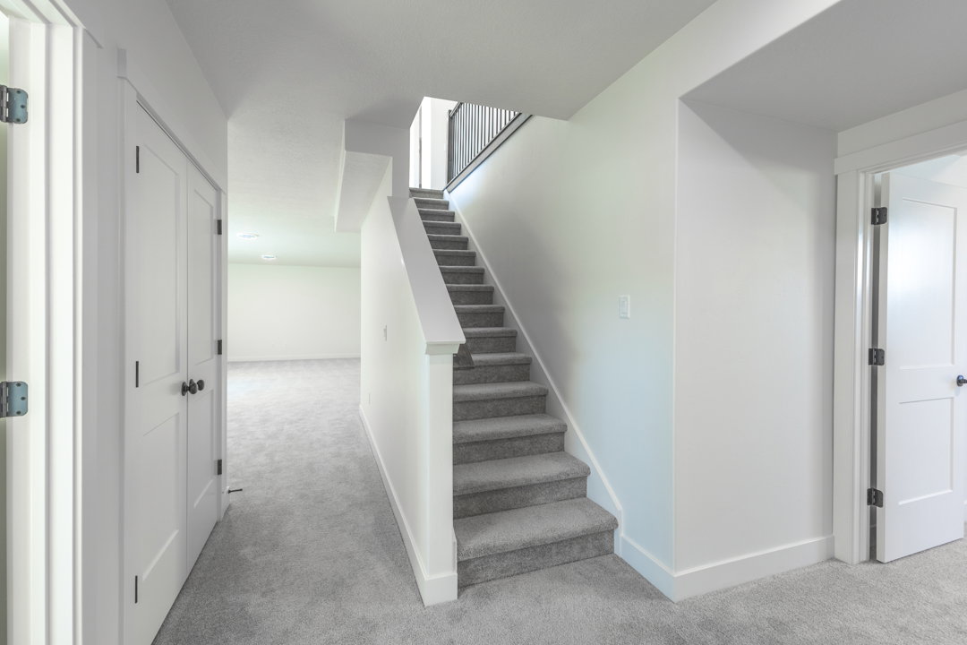Carpeted staircase with black metal balusters, white baseboards, and white walls