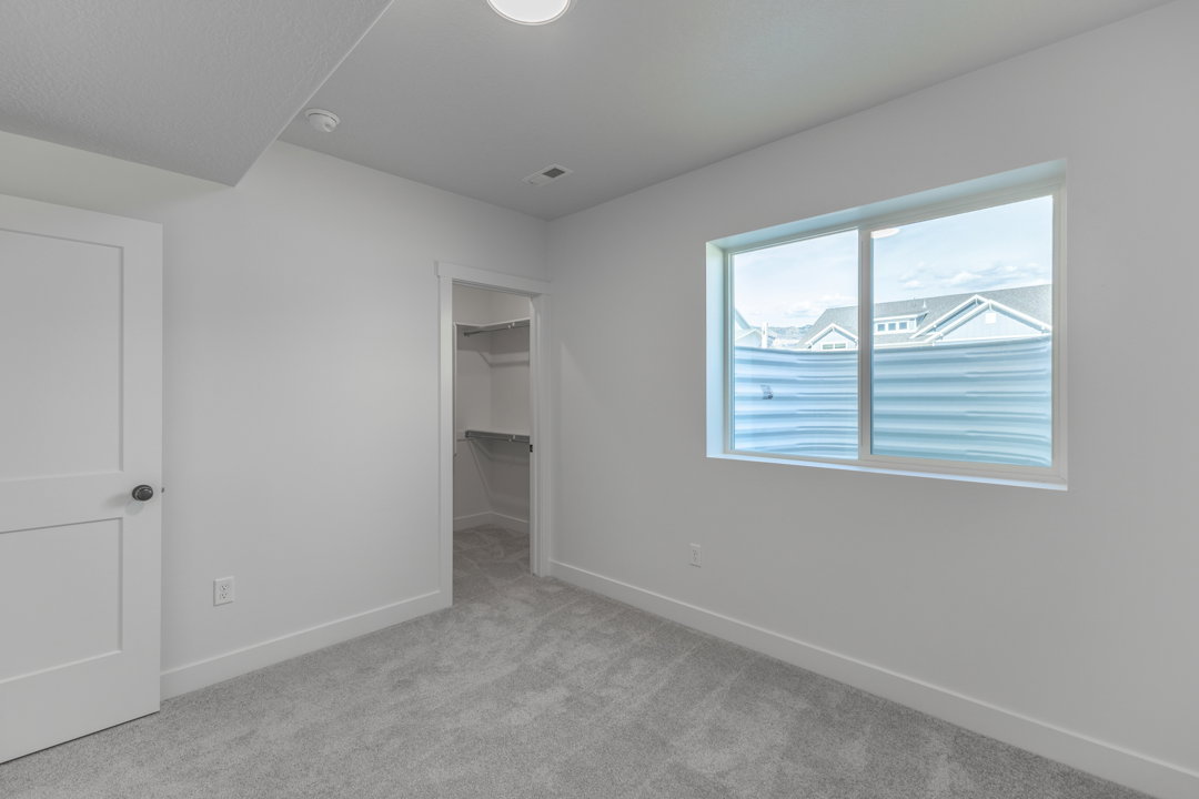 Room featuring light gray carpeting, crisp white walls, a single window with a privacy blind, and an open closet with built-in shelving