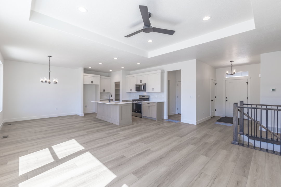 Open-concept living space featuring wood-finish flooring, a tray ceiling with recessed lighting and a ceiling fan, and a kitchen island with a sink and modern faucet