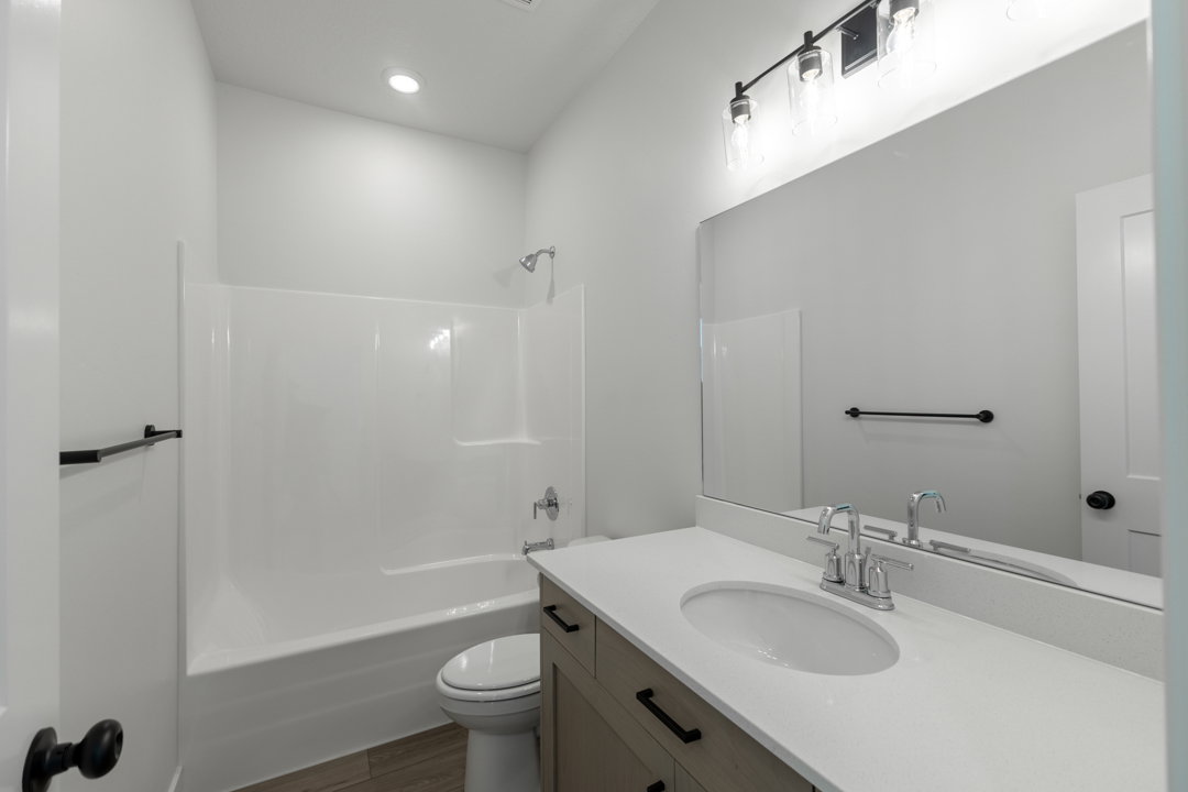 Bathroom featuring a light wood-finish vanity with a white countertop and undermount sink, a large wall-mounted mirror, and a white tub/shower combination