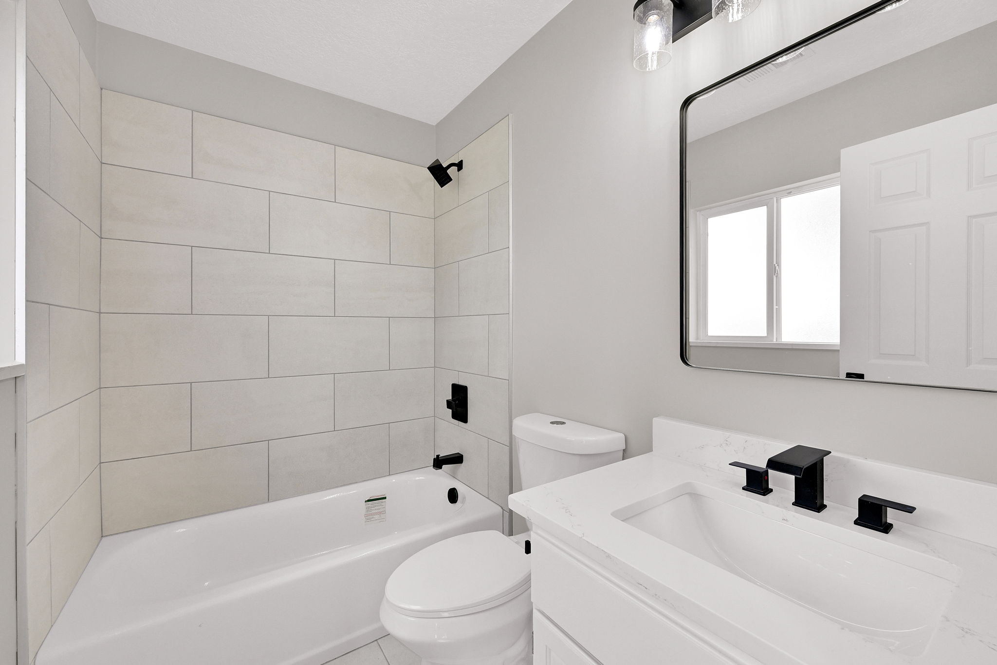 Bathroom featuring a white vanity with an integrated sink, matte black fixtures, a rectangular framed mirror, and a white subway-tiled shower surround