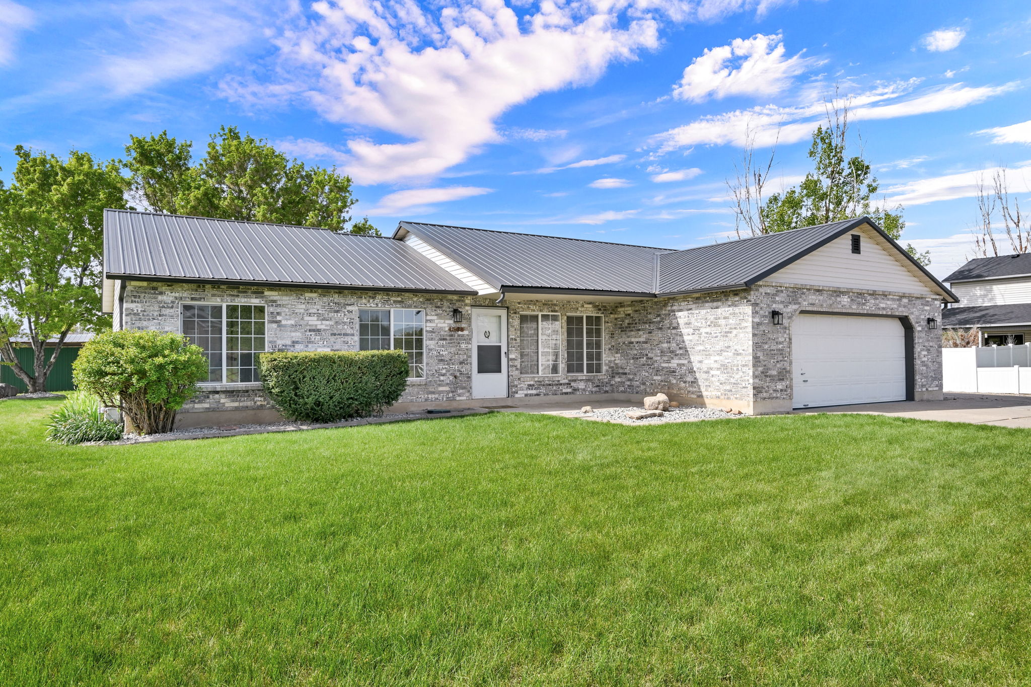 Stone veneer exterior featuring a metal roof, attached two-car garage, and established landscaping