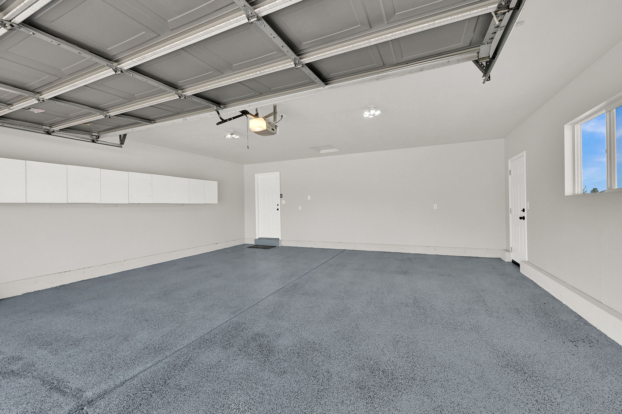 Spacious garage featuring a durable epoxy-coated floor, automatic garage door opener, white wall-mounted cabinetry, recessed lighting, and a white interior door