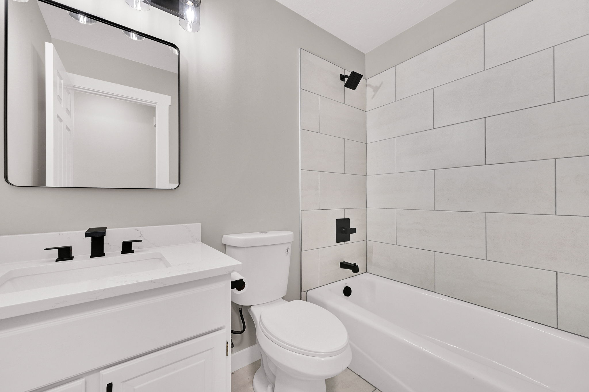 Contemporary bathroom featuring a white vanity with integrated sink, black hardware, a rectangular mirror, and a tiled shower/tub combination with black fixtures