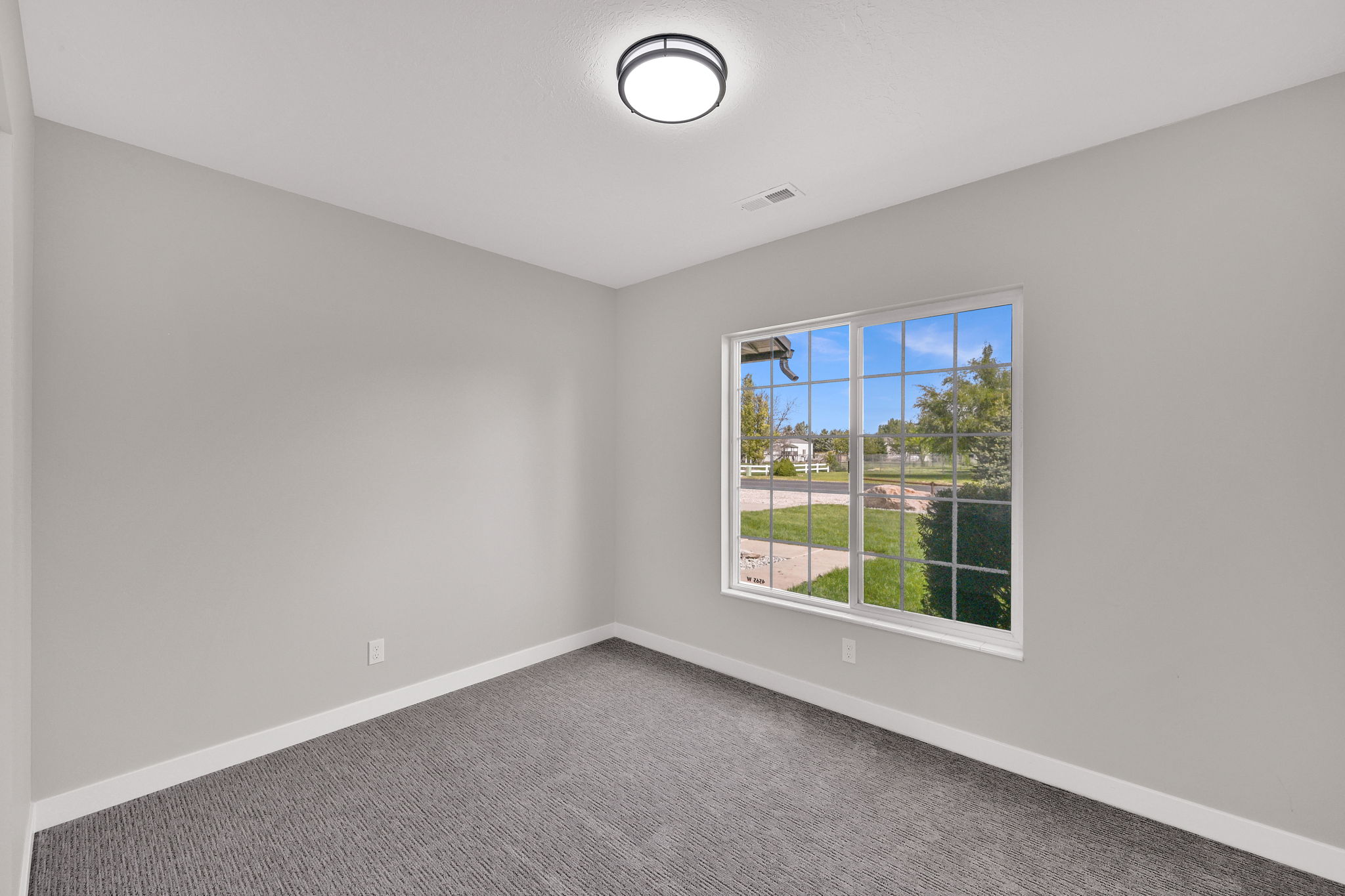 Neutral-toned room featuring a large window, patterned carpet flooring, white baseboards, and a flush-mount ceiling light