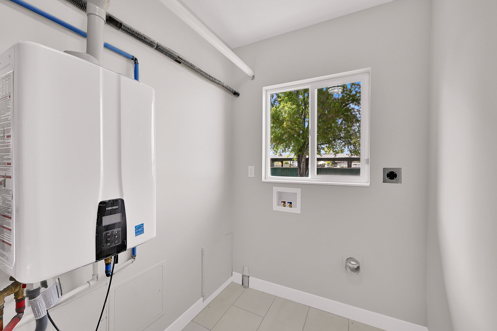 Utility room featuring a tankless water heater, white framed window, and light tile flooring