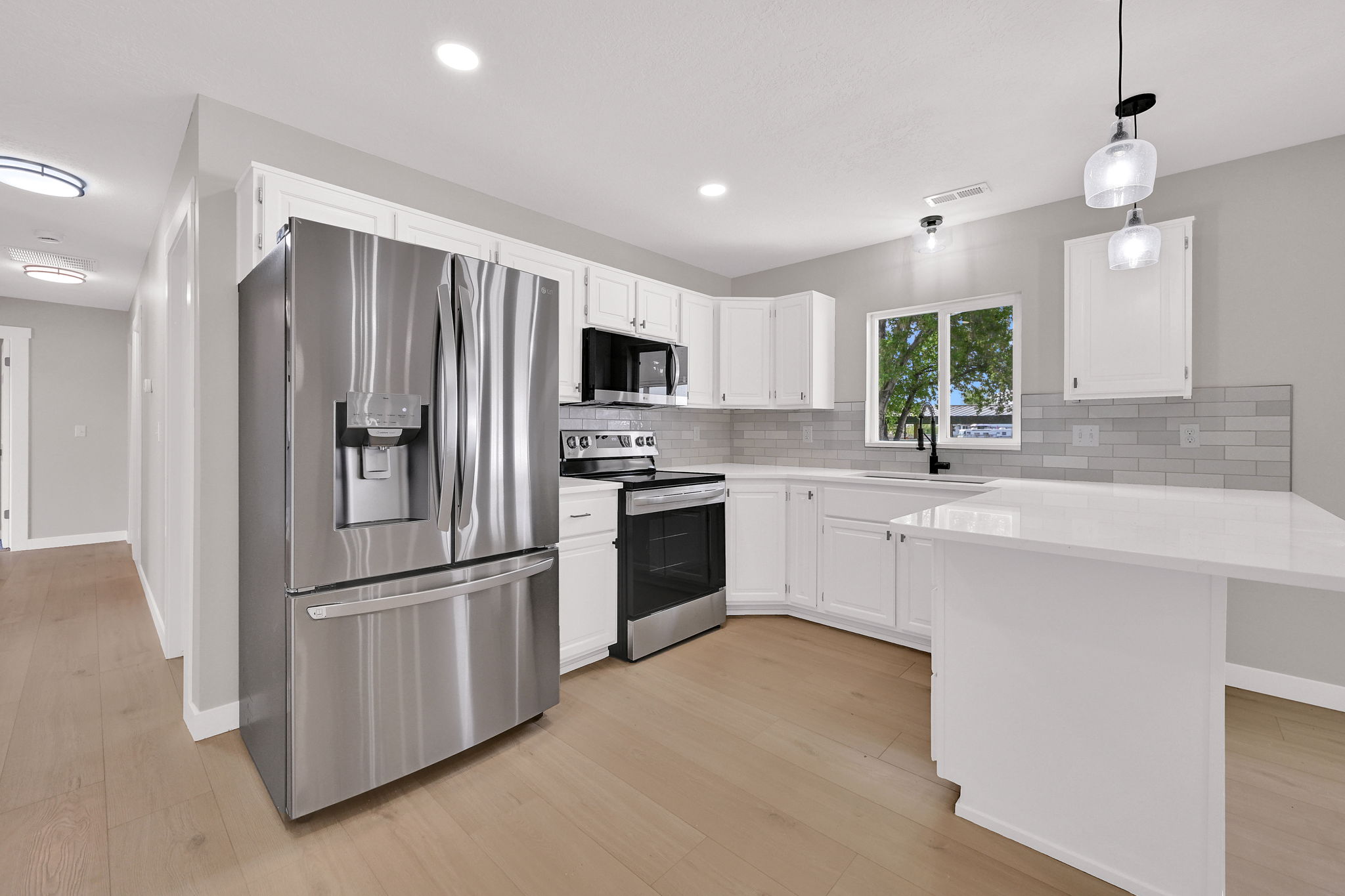 Kitchen featuring stainless steel appliances, white cabinetry, light-toned wood-finish flooring, and a subway tile backsplash