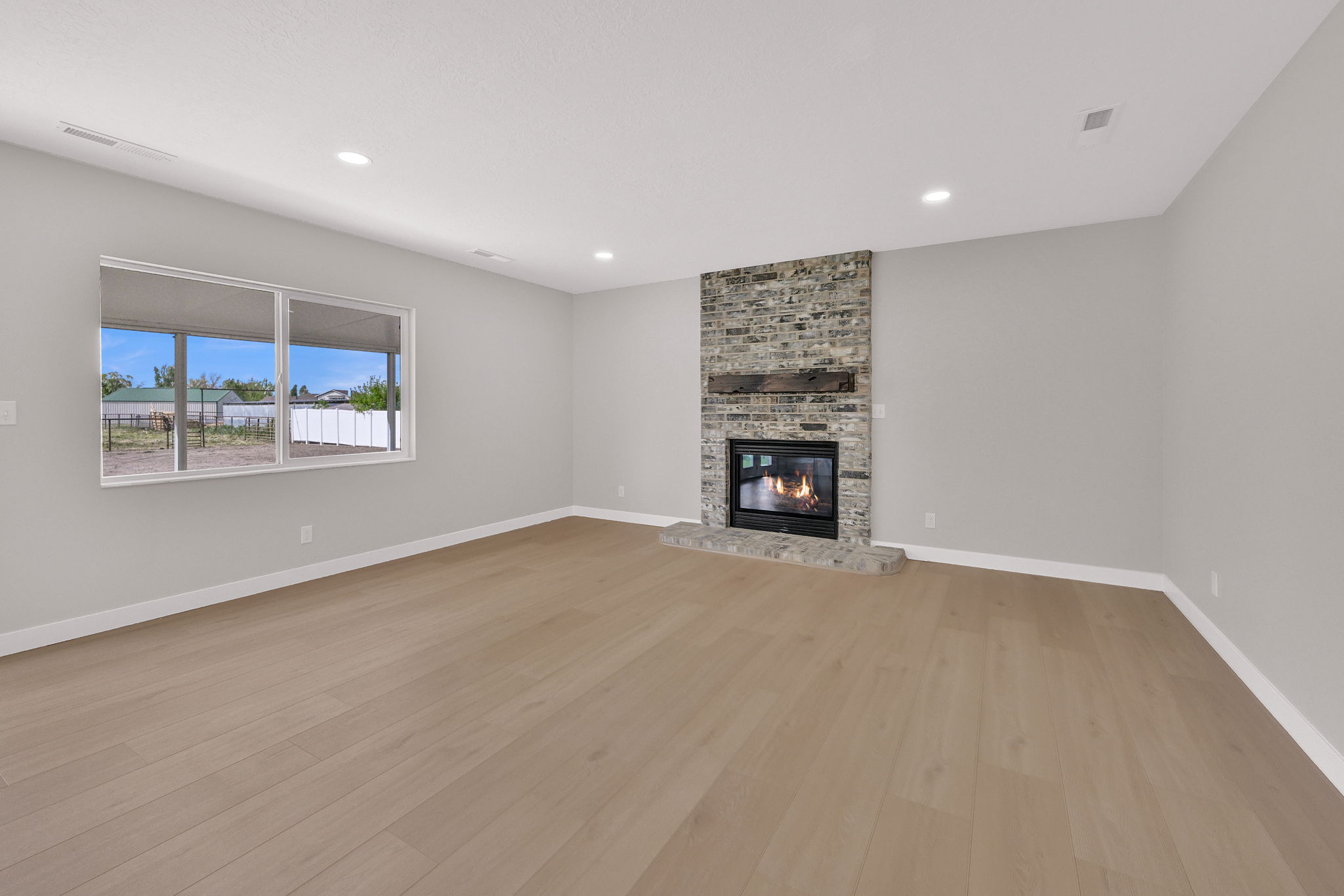 Spacious living area featuring a gray brick fireplace with a wood mantel, light wood-finish flooring, recessed lighting, and a large window