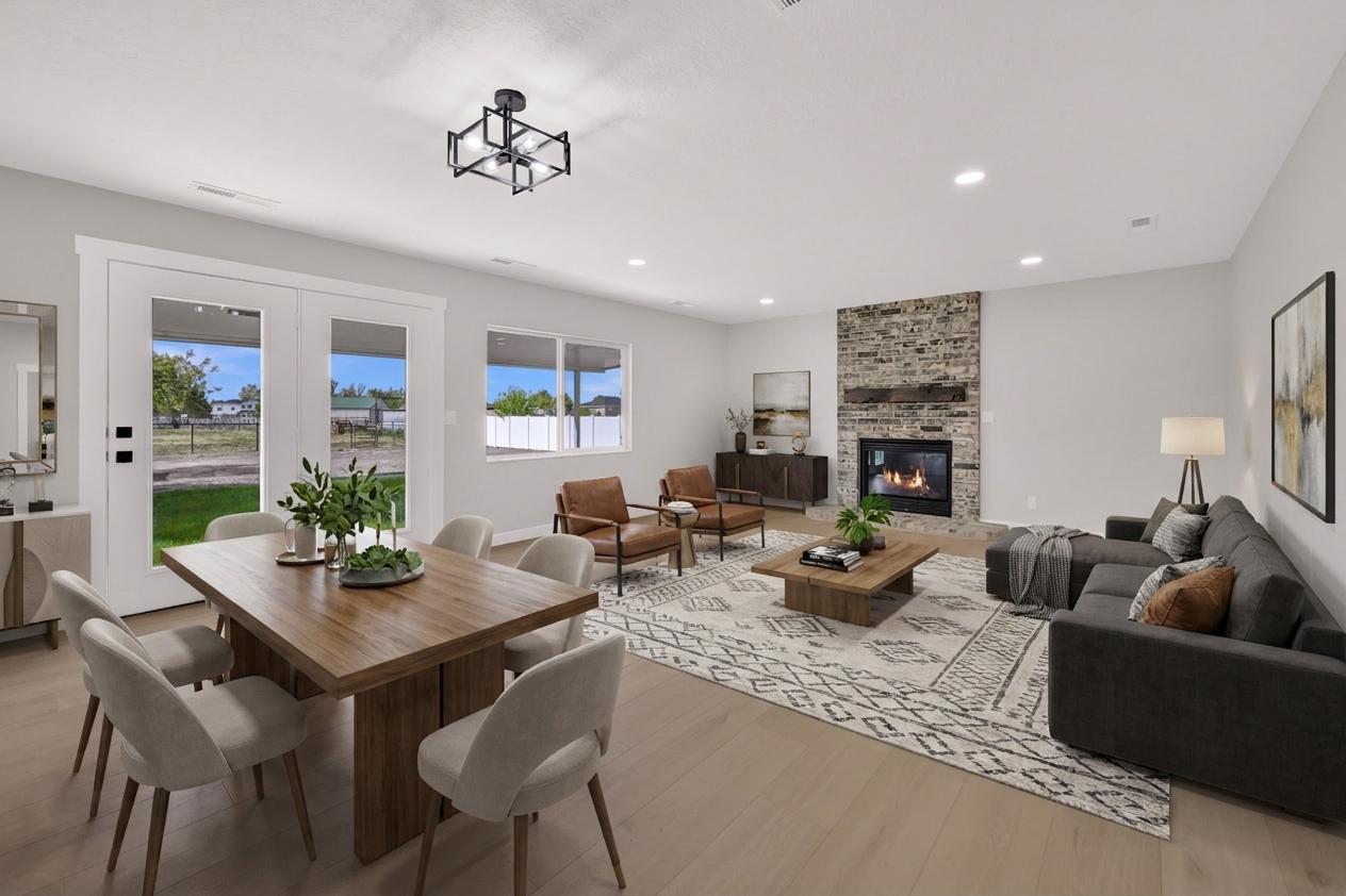 Open-concept living area featuring light wood-finish flooring, a stone-clad fireplace with a hearth, recessed lighting, and a modern ceiling fixture
