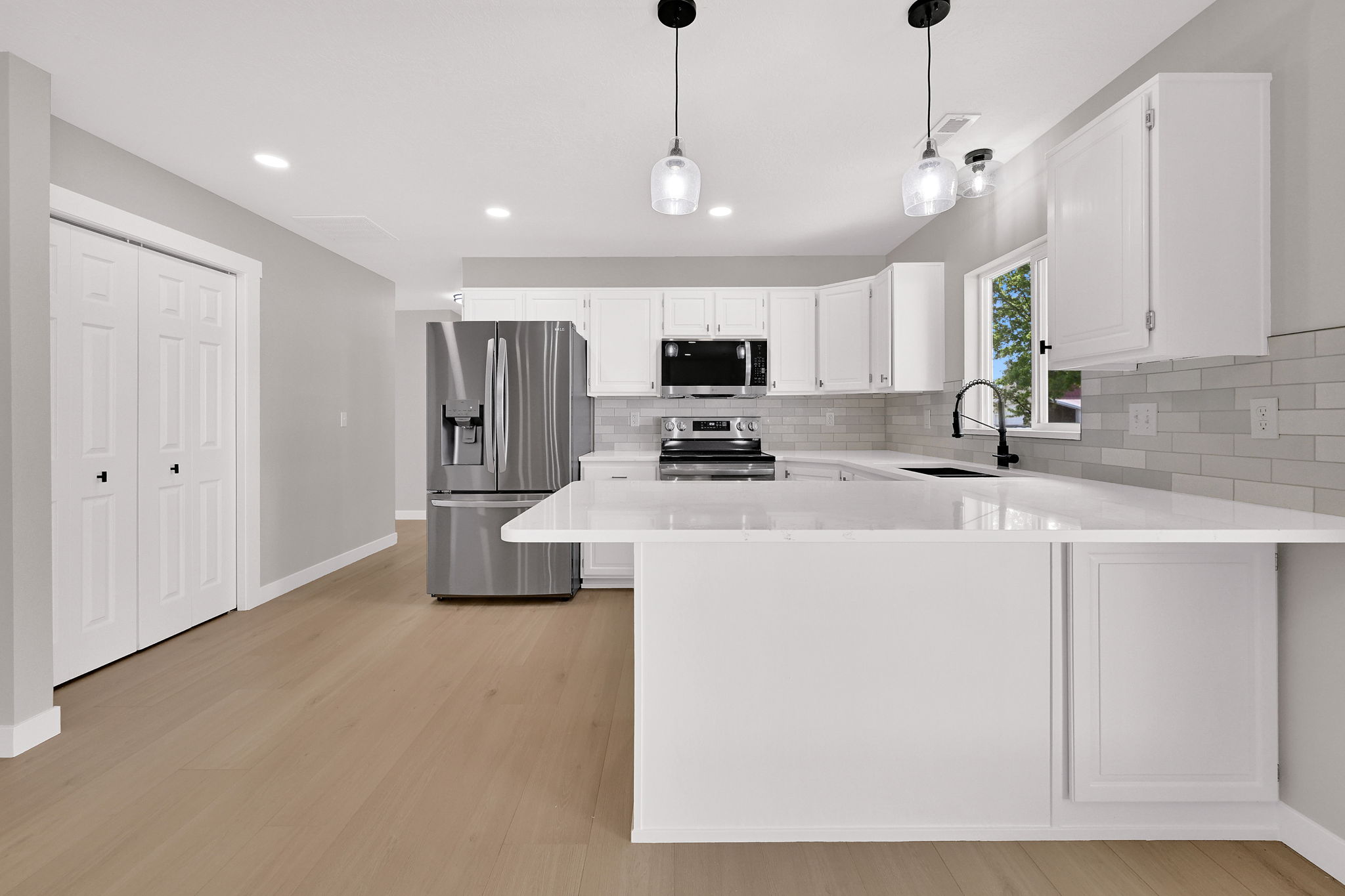Contemporary kitchen featuring white cabinetry, light-toned wood-finish flooring, stainless steel appliances, a white subway tile backsplash, and a breakfast bar