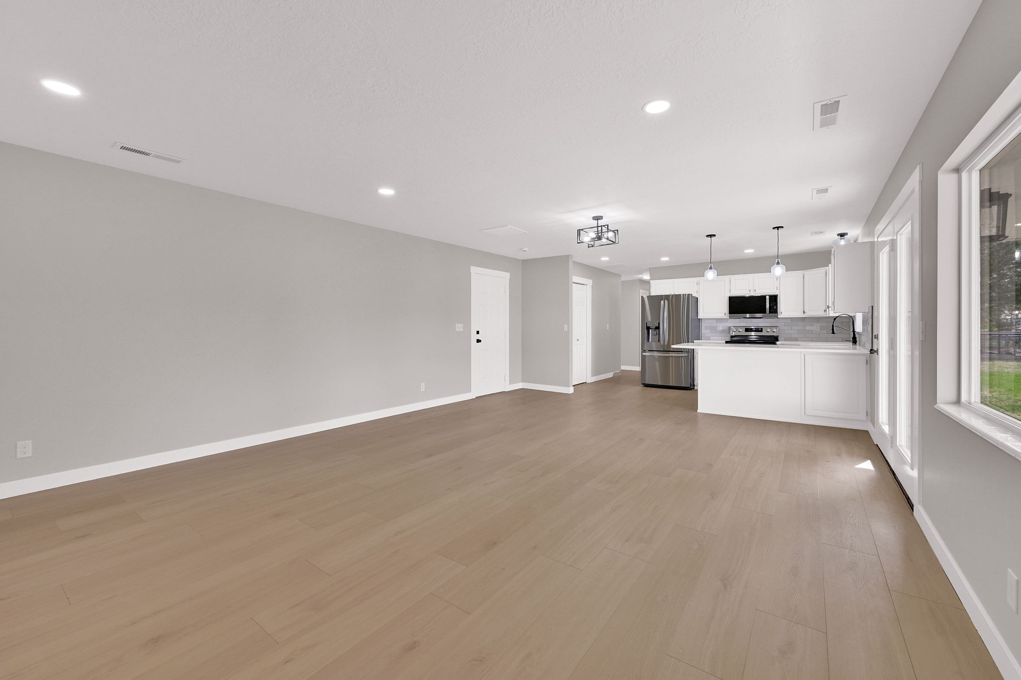Open-concept living area featuring light wood-finish flooring, recessed lighting, and a modern kitchen