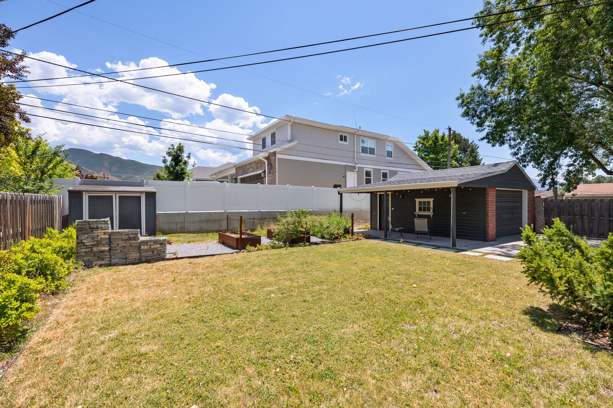 Spacious backyard featuring a detached garage with covered patio, wood fencing, a storage shed, and a stone-clad fire pit area