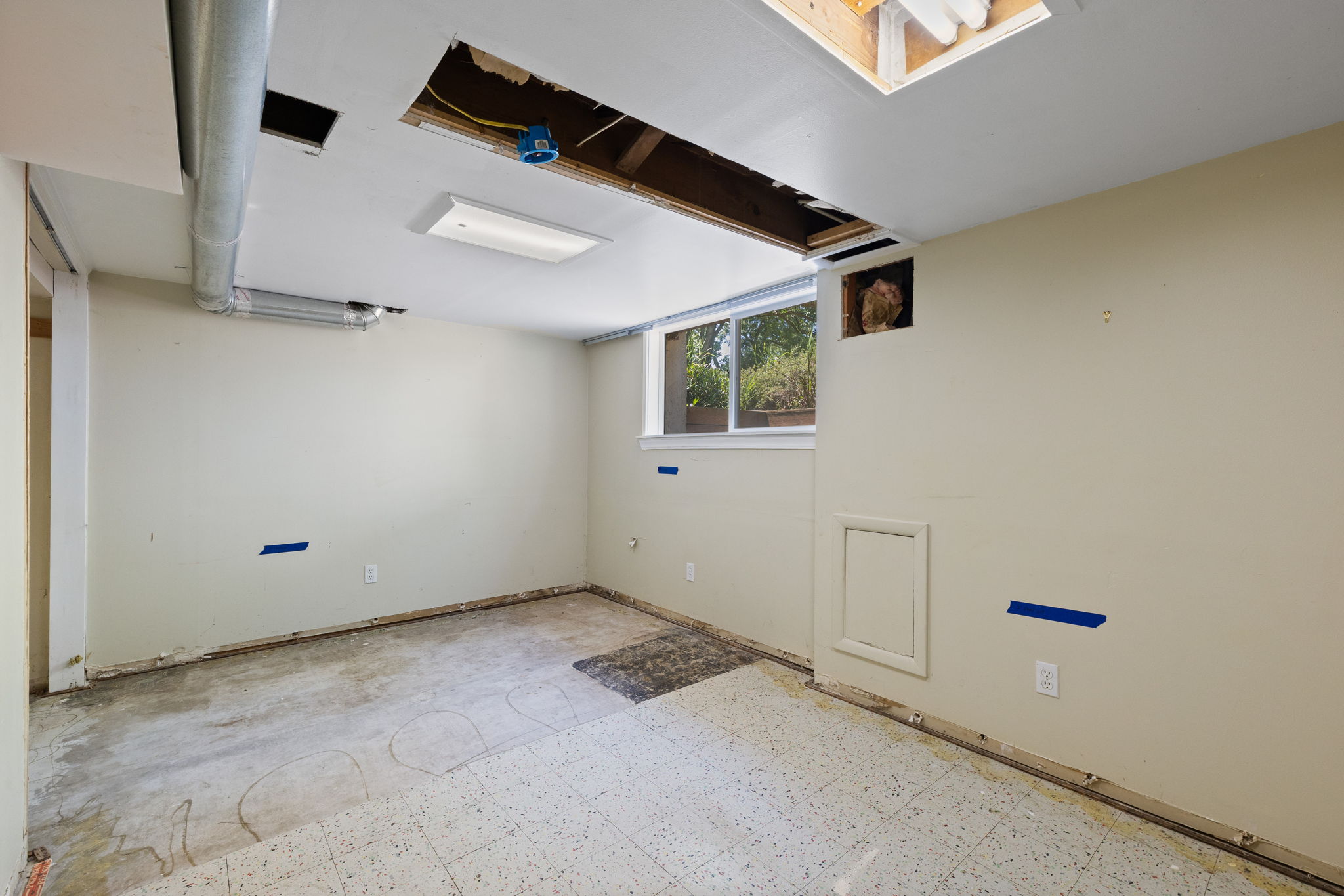 Room featuring a window, built-in access panel, exposed ceiling joists, and a utility conduit