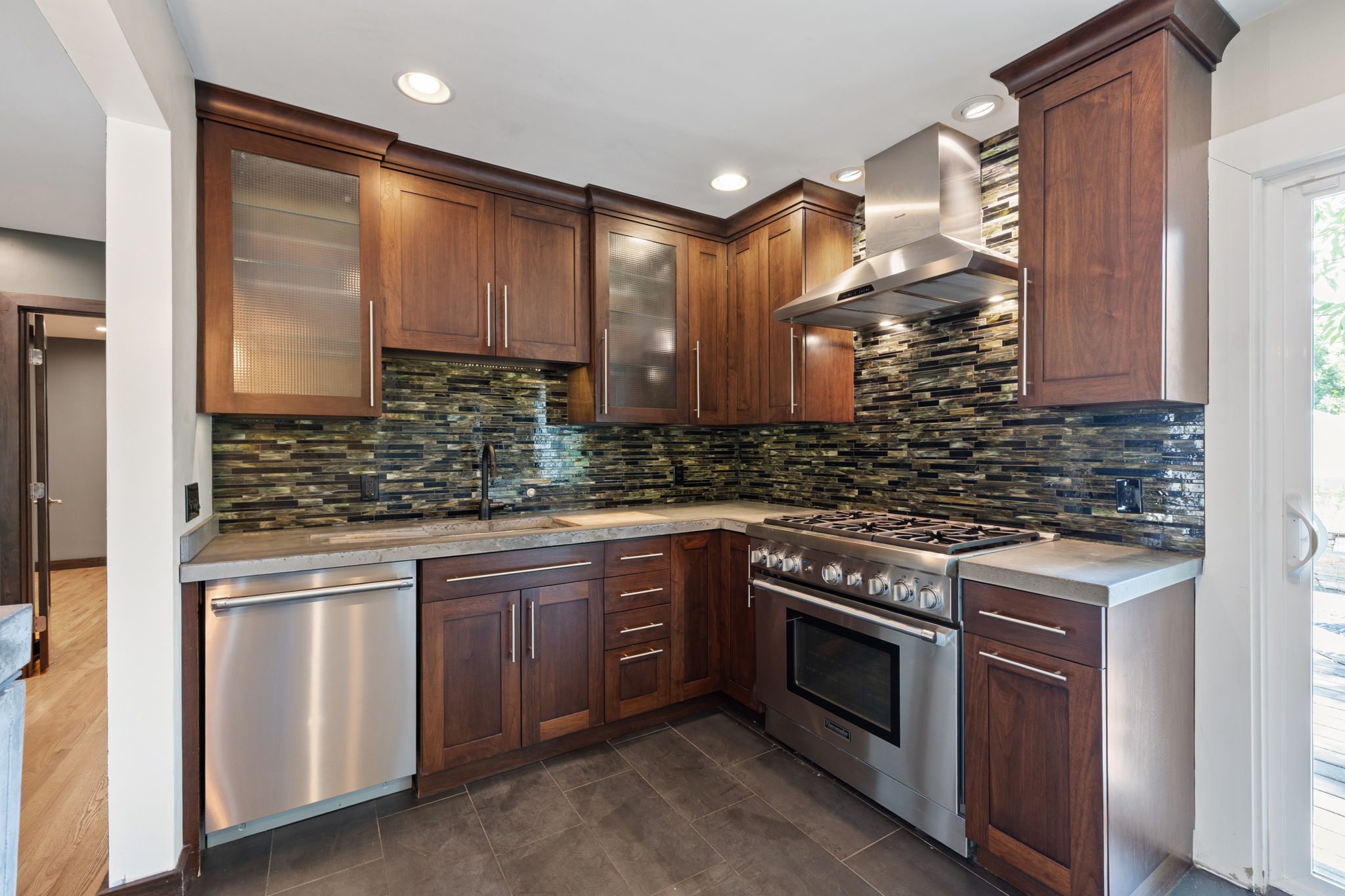 Kitchen featuring rich wood cabinetry, stainless steel appliances, a mosaic tile backsplash, composite countertops, and recessed lighting