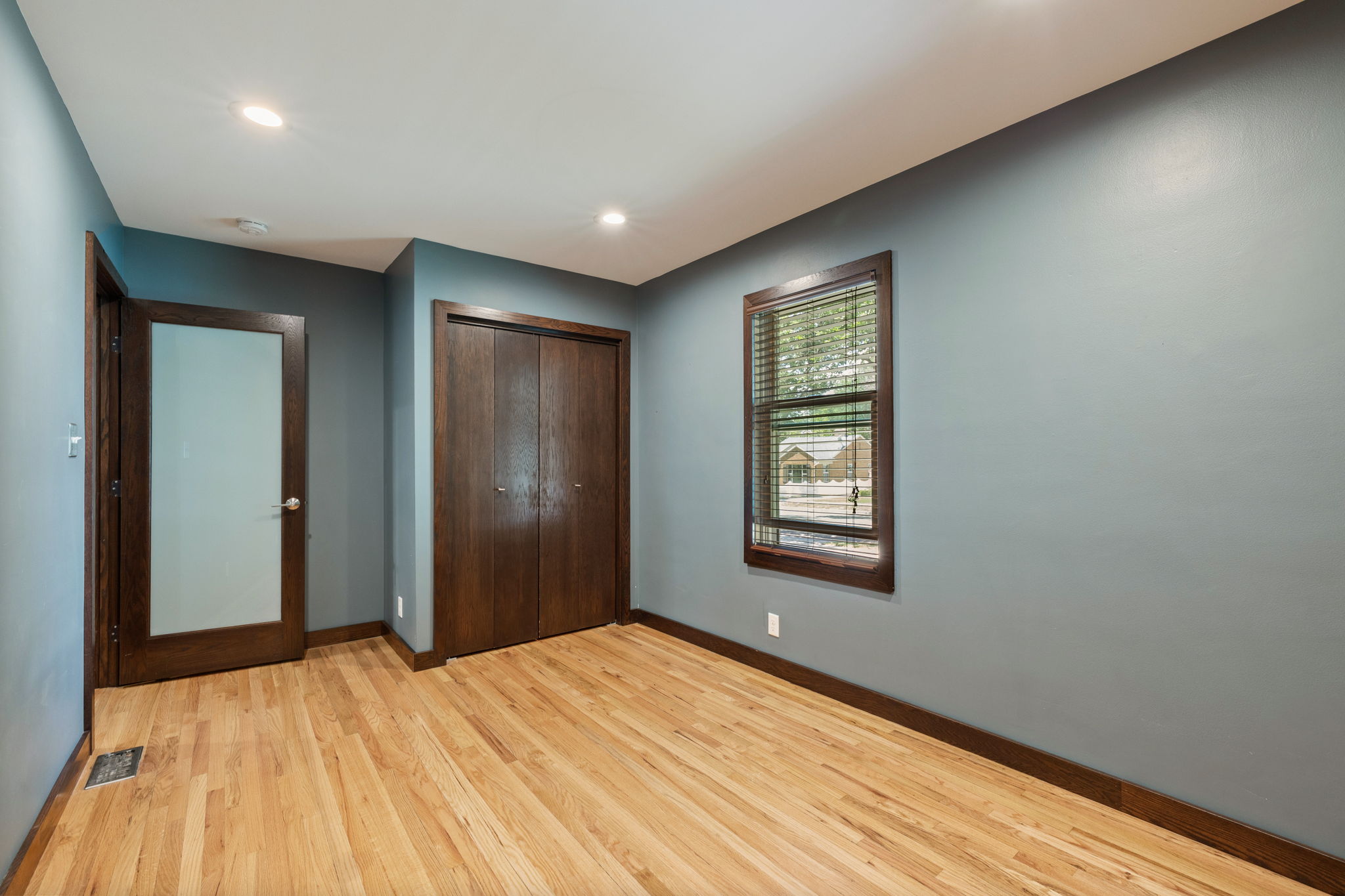 Hardwood flooring extending throughout, complemented by a bi-fold closet and a contemporary door with frosted glass