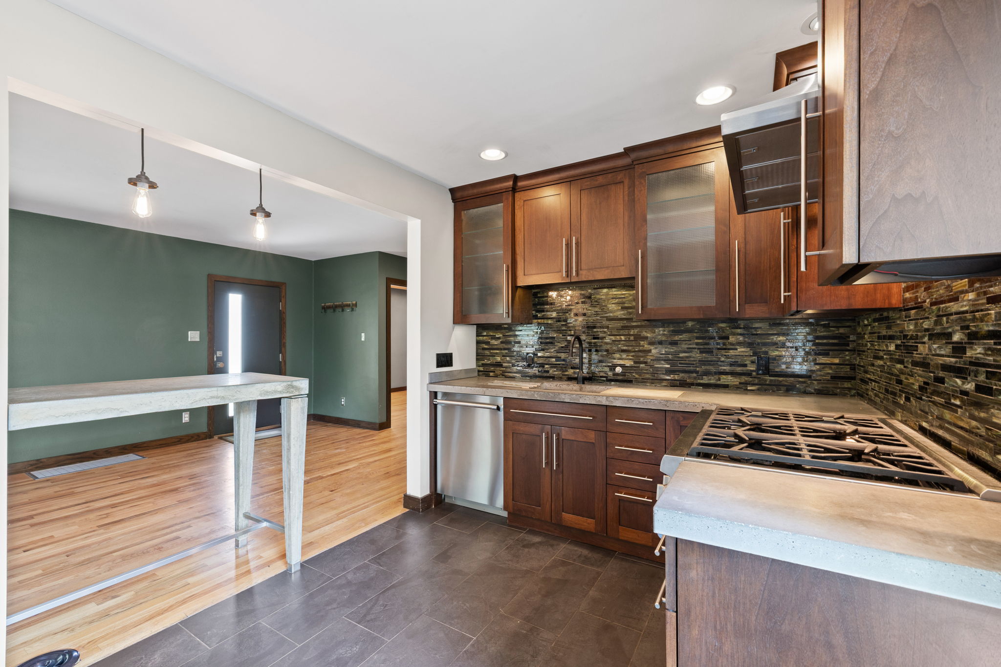 Modern kitchen featuring wood cabinetry, stone countertops, a mosaic tile backsplash, and stainless steel appliances