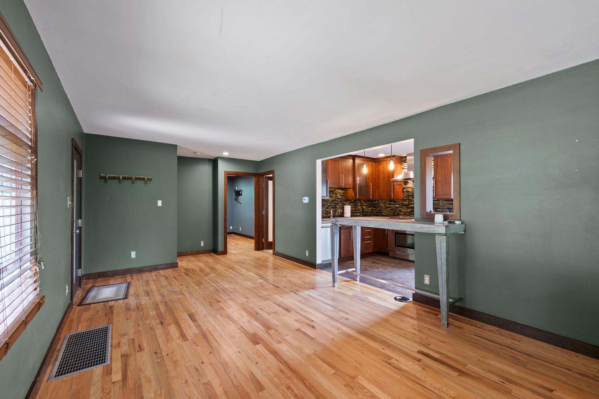Open-concept living area with wood-finish flooring, a pass-through kitchen window, and a built-in breakfast bar