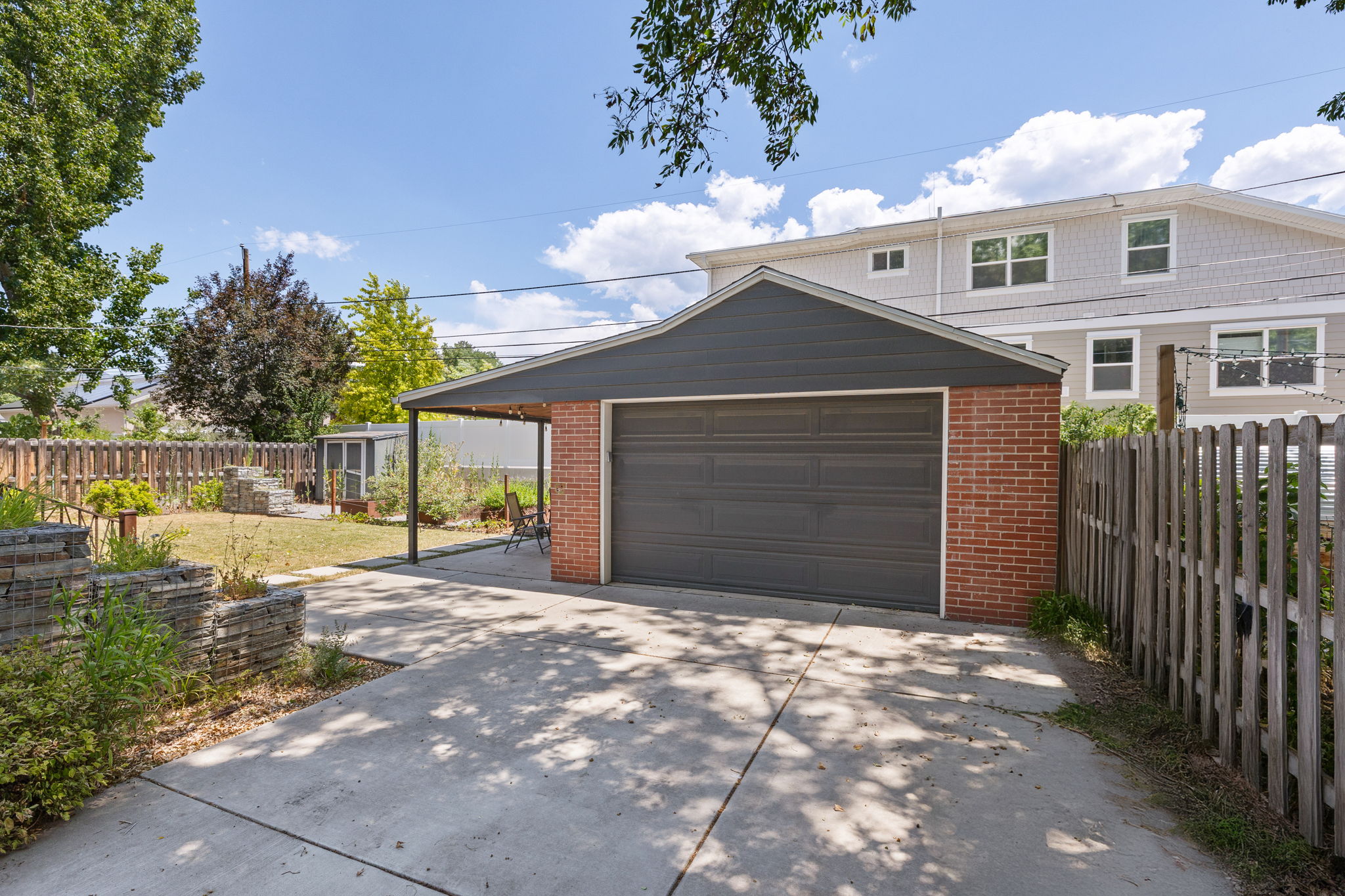 Detached garage featuring brick and dark siding, a dark garage door, and an attached covered patio