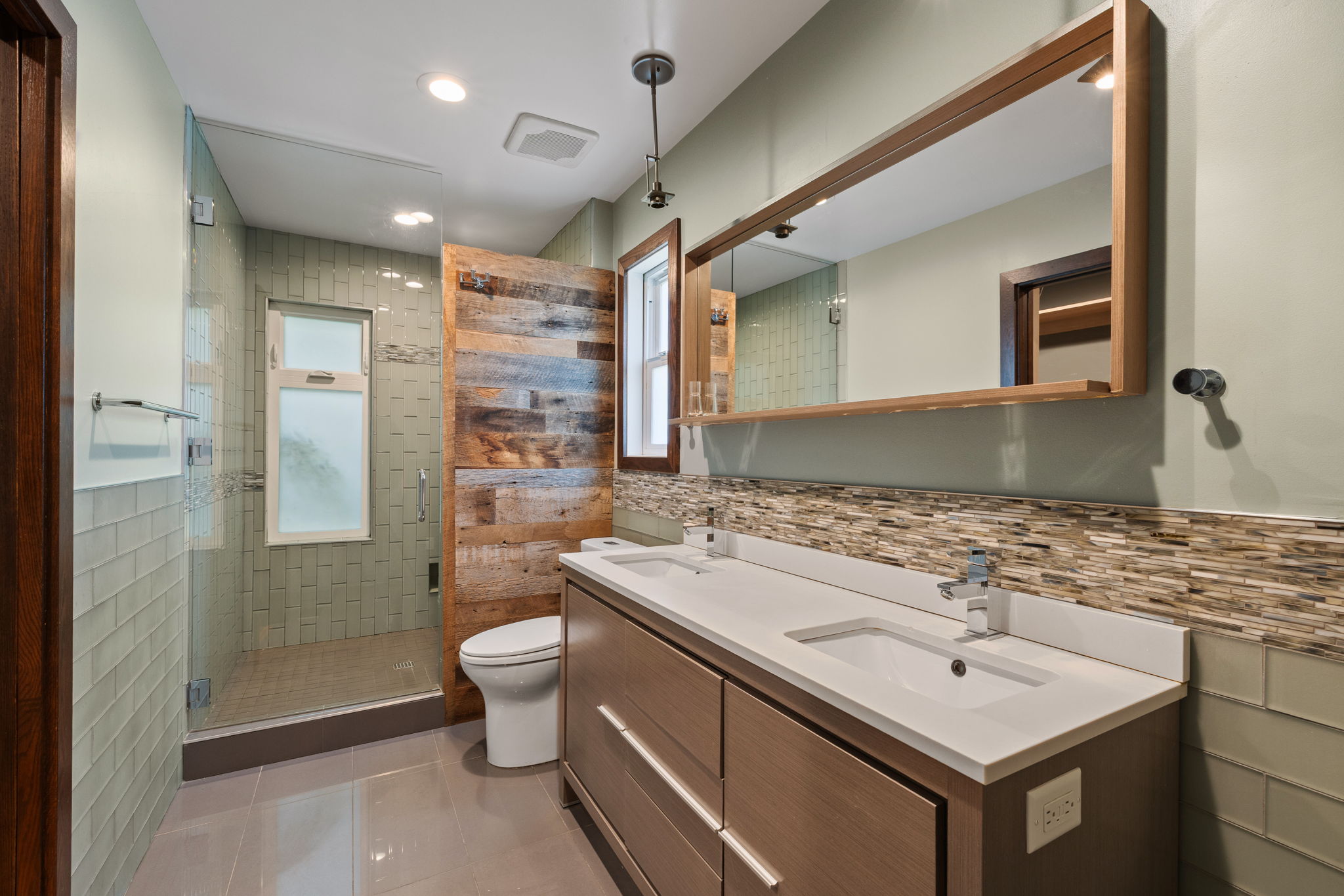 Bathroom featuring a dual-sink vanity with white countertops, a large framed mirror, and a glass-enclosed shower