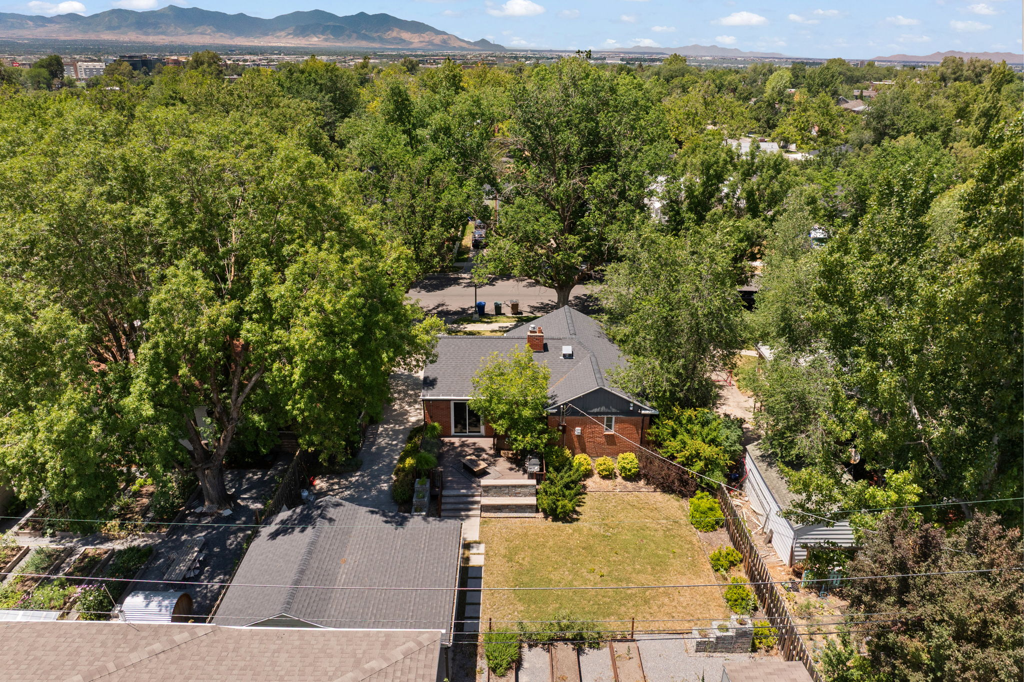 Brick exterior home featuring a dark roof, mature tree canopy, and a green lawn