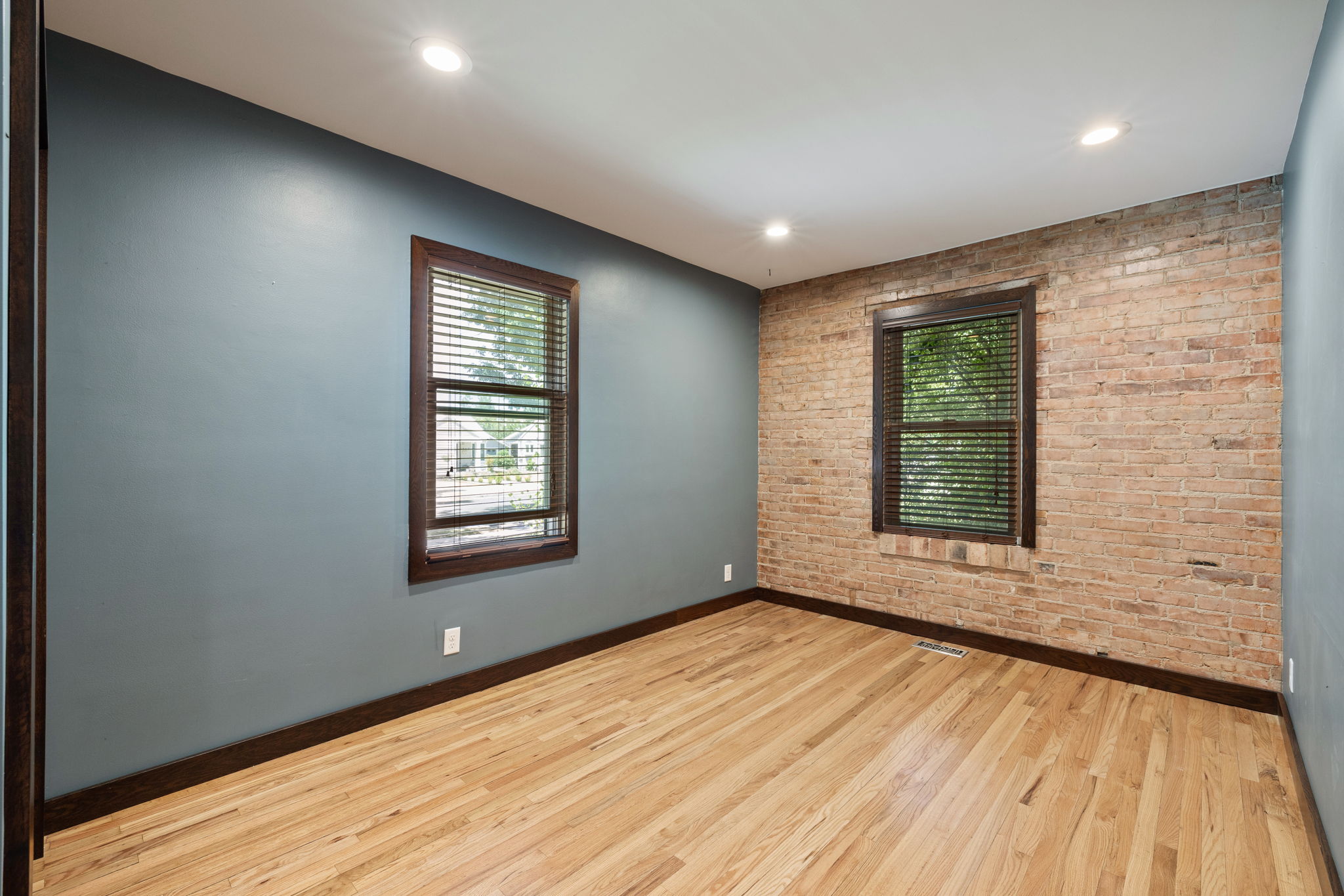 Exposed brick accent wall with two windows, light wood-finish flooring, recessed lighting, and dark trim
