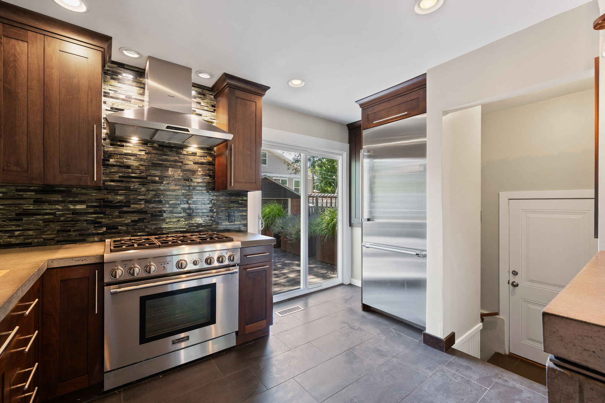 Modern kitchen featuring dark wood cabinetry, stainless steel appliances, a textured tile backsplash, and light-colored countertops
