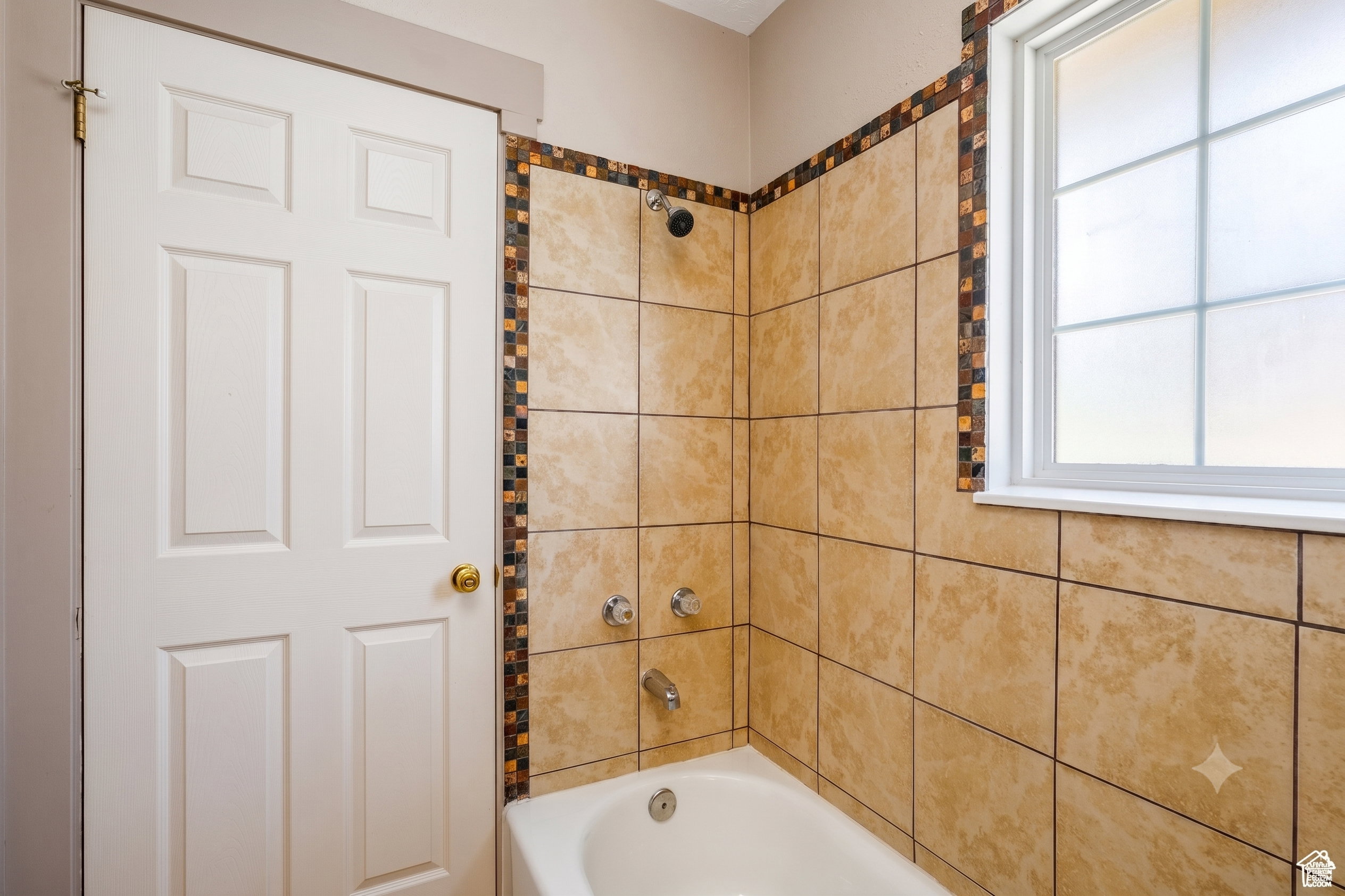 Bathtub with a tiled surround featuring decorative mosaic accents