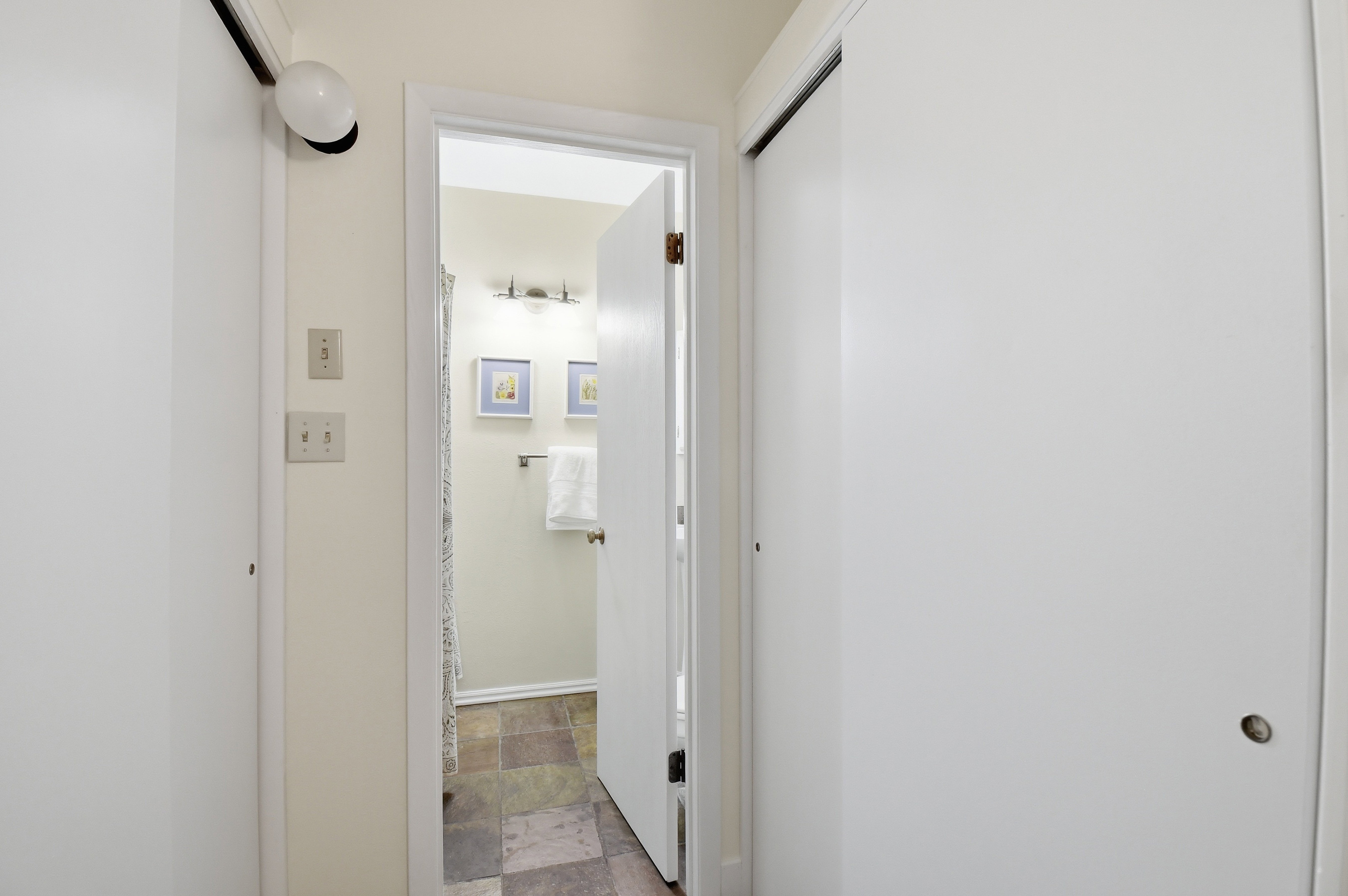 Hallway entrance featuring two white sliding closet doors, wall-mounted light fixture, and light switches