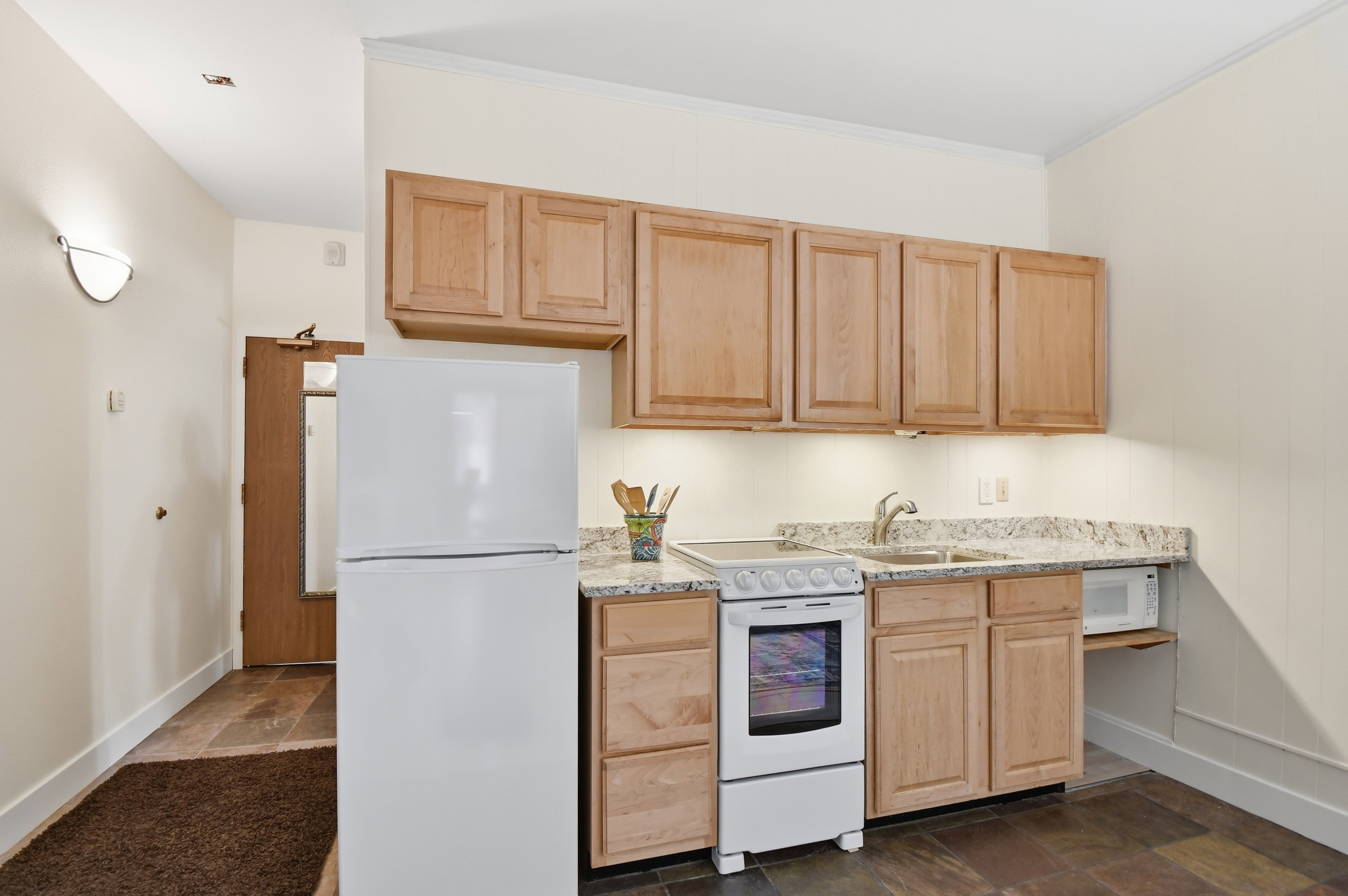 Compact kitchen featuring light wood-finish cabinetry, granite-style countertops, and a full suite of white appliances