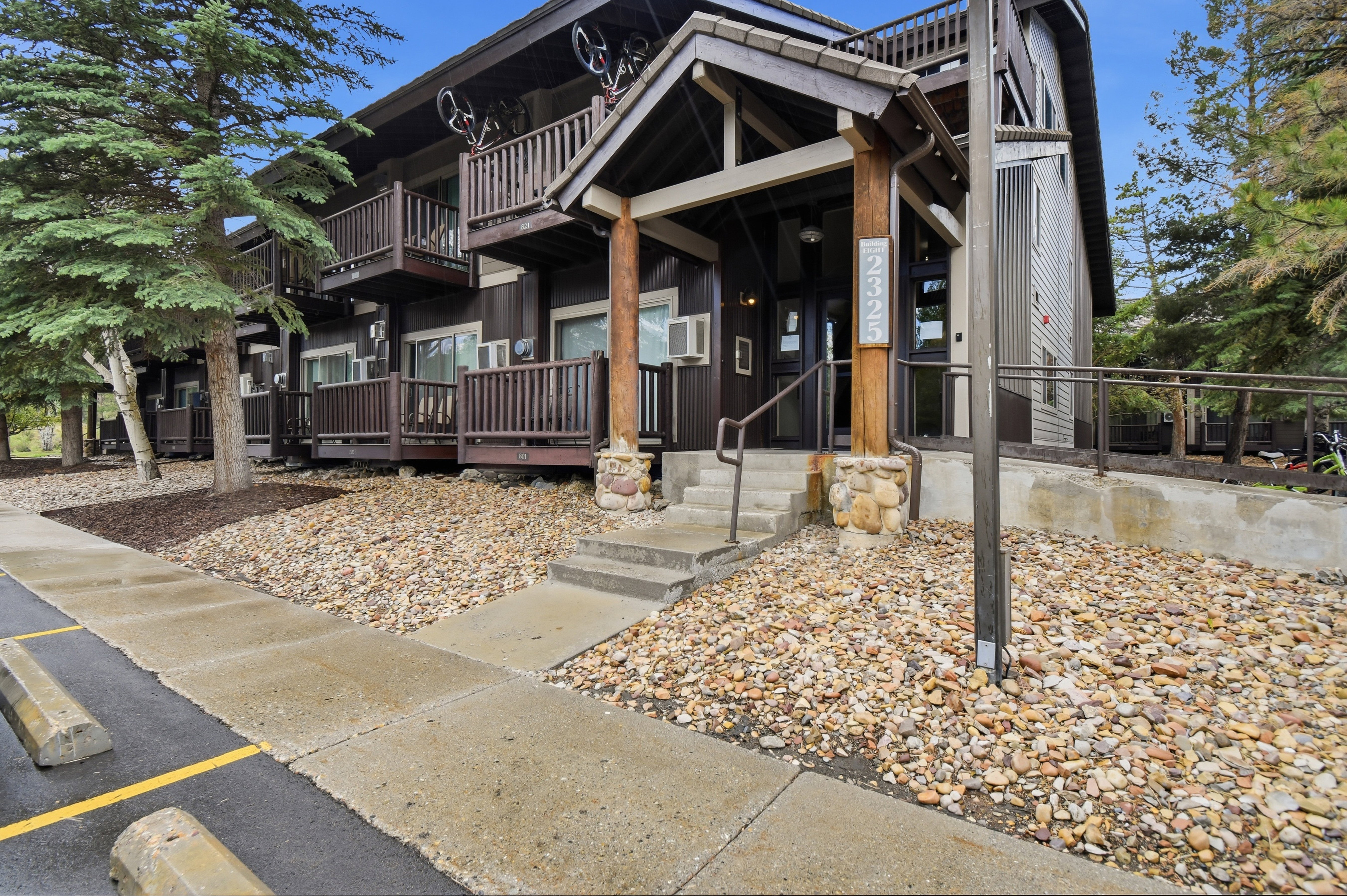 Multi-story building featuring dark wood siding, multiple private balconies with wood railings, and a stone-accented entry