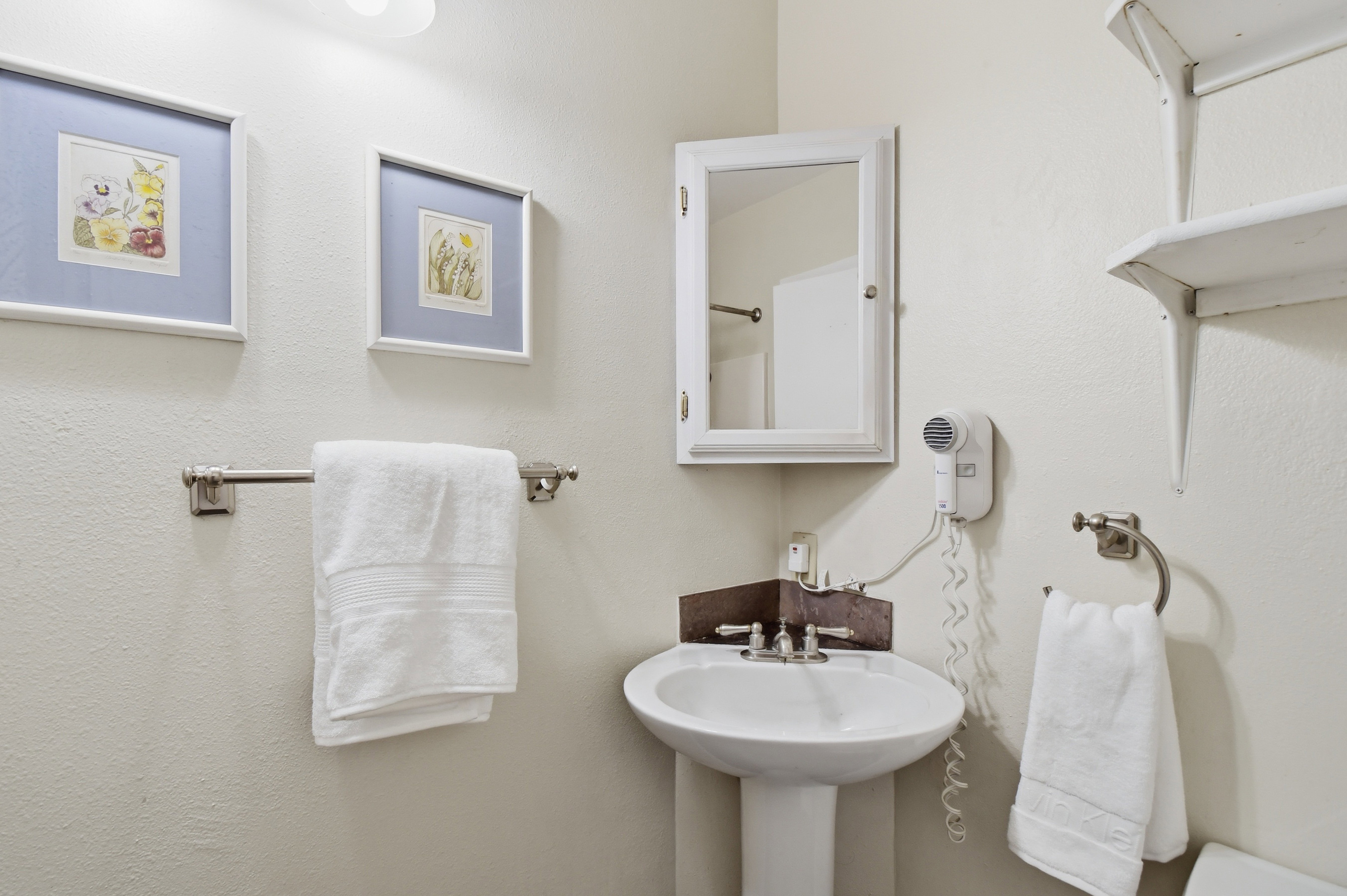 Pedestal sink with chrome-finish fixtures, wall-mounted medicine cabinet, and open shelving
