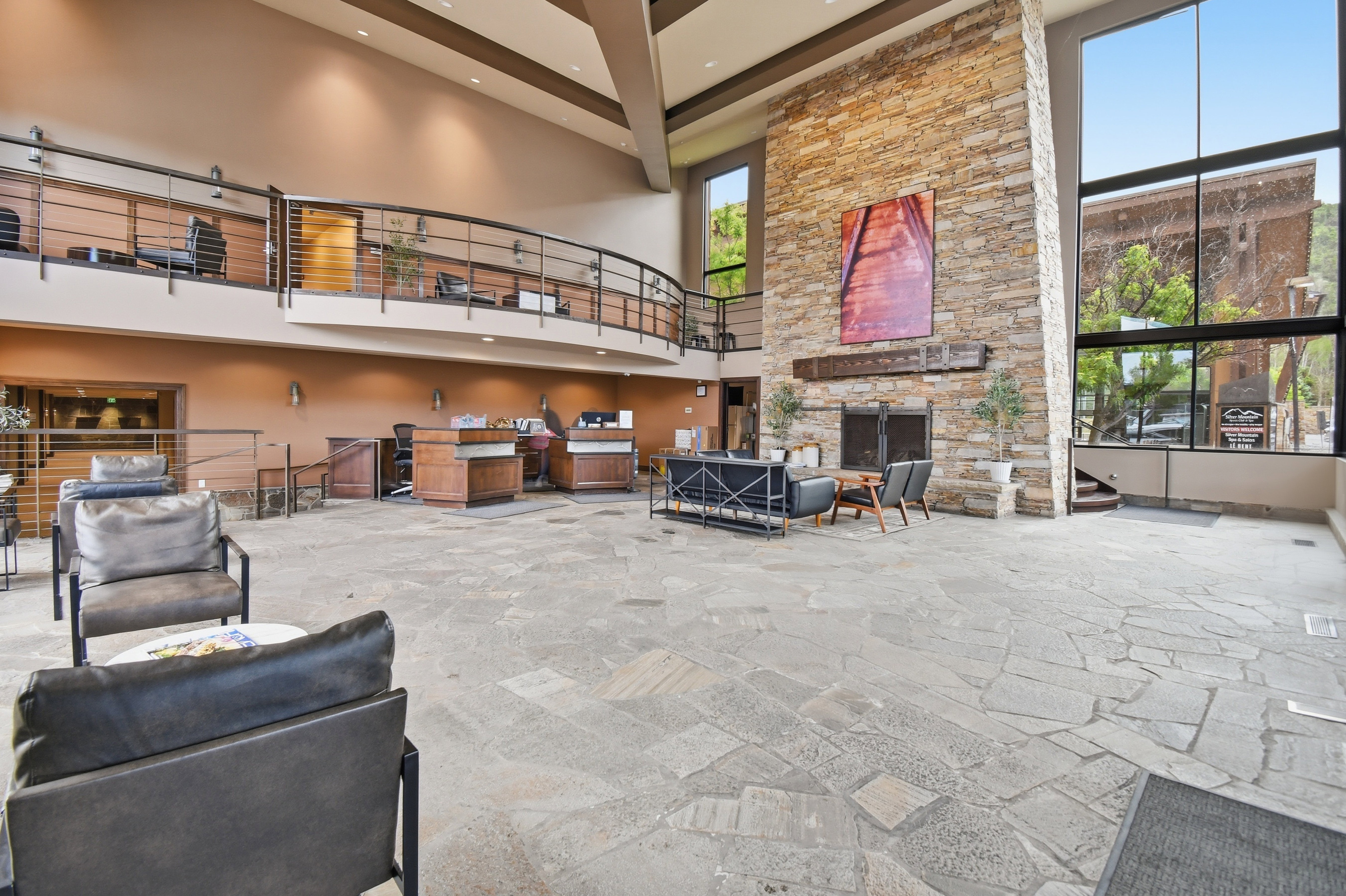 Spacious foyer with flagstone flooring, a two-story stone fireplace, expansive window walls, and a visible mezzanine with metal railings