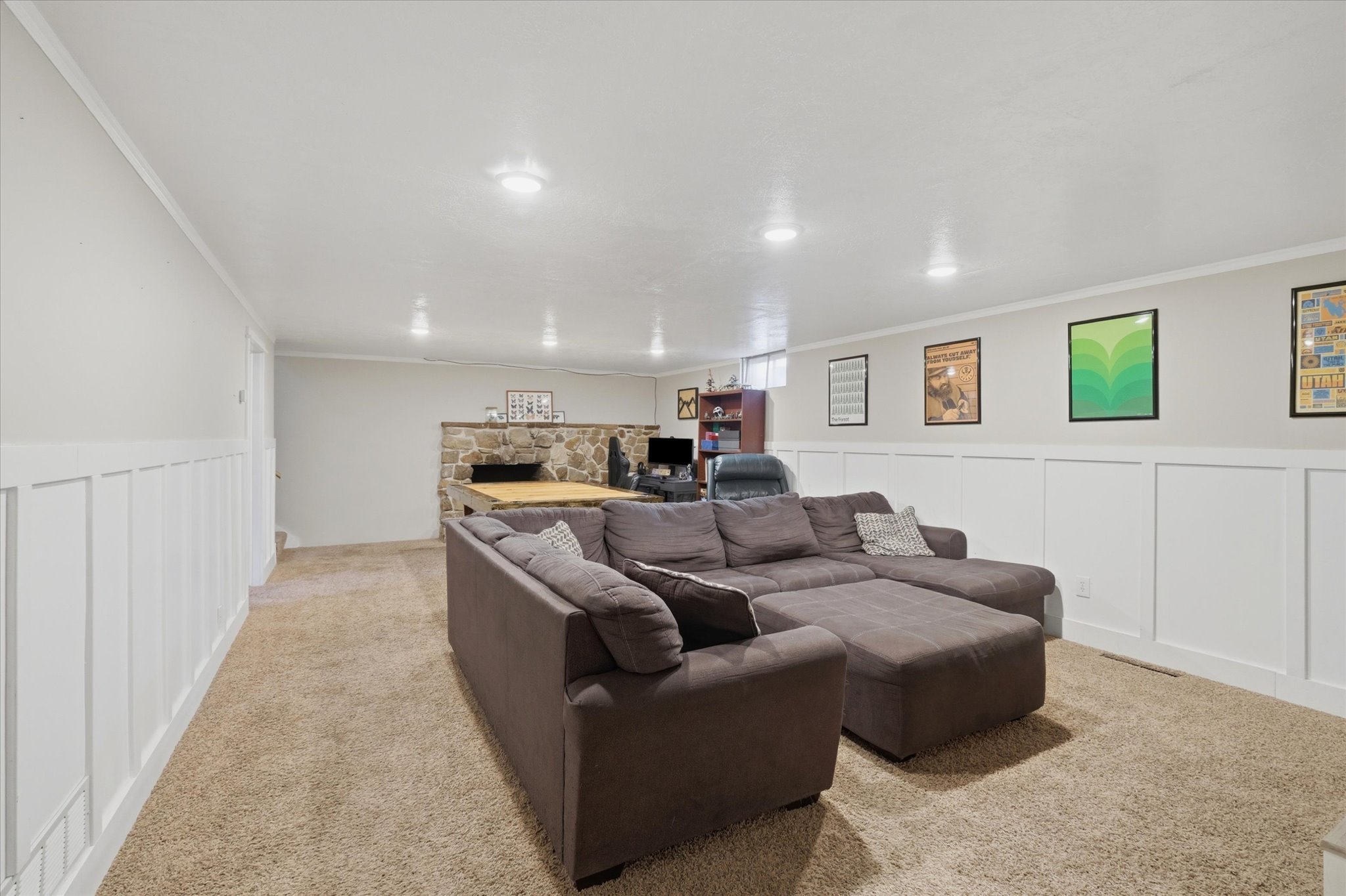 Spacious room featuring light-colored carpeting, white wall paneling, recessed lighting, and a stone-faced bar area