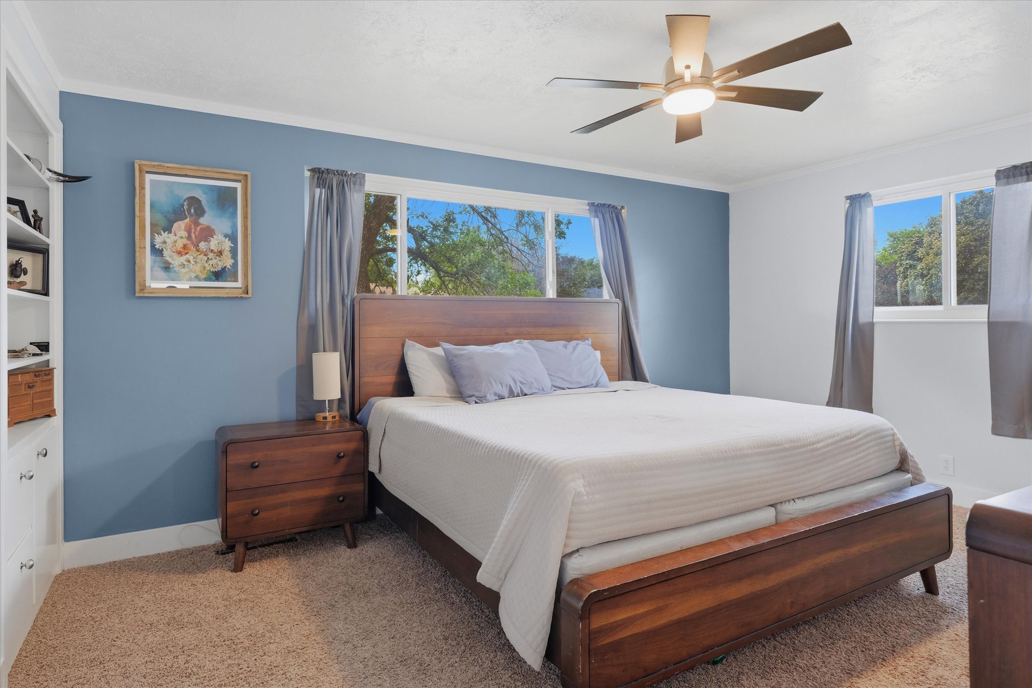 Bedroom featuring a built-in bookshelf, multiple windows, a ceiling fan with integrated lighting, and crown molding