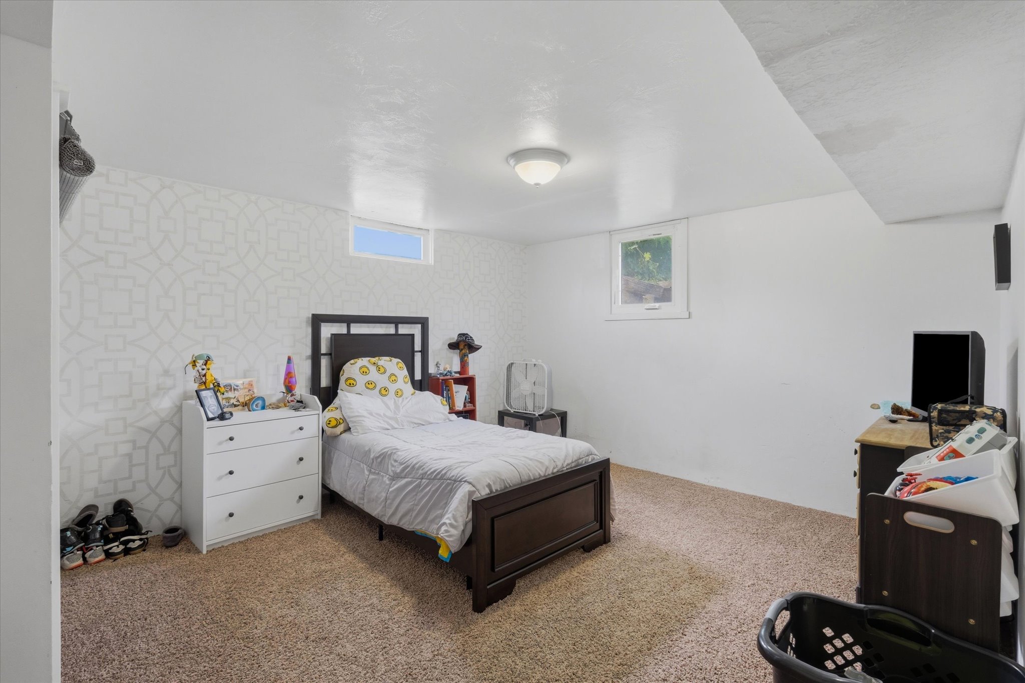 Carpeted room featuring a patterned accent wall, white painted walls, and a white ceiling with a flush-mount light fixture