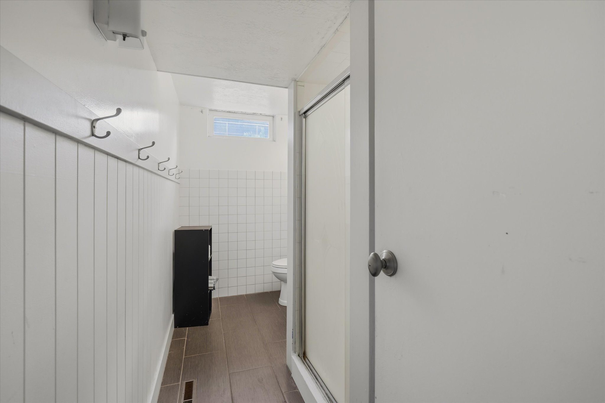 White paneled wall with metal hooks, wood-finish flooring, and white tiled walls