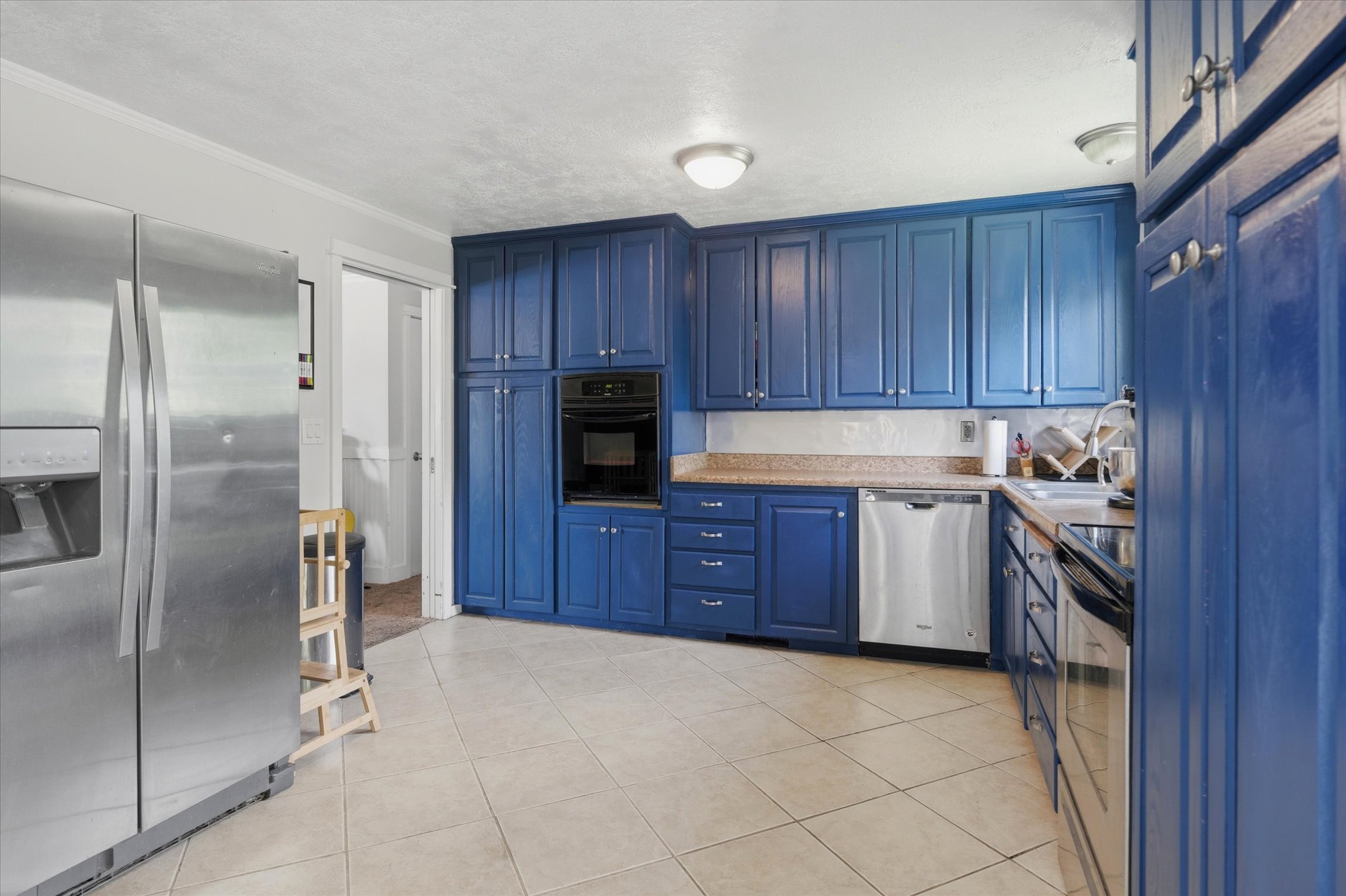 Kitchen featuring custom blue cabinetry, light tile flooring, built-in oven, stainless steel dishwasher, and a stainless steel side-by-side refrigerator