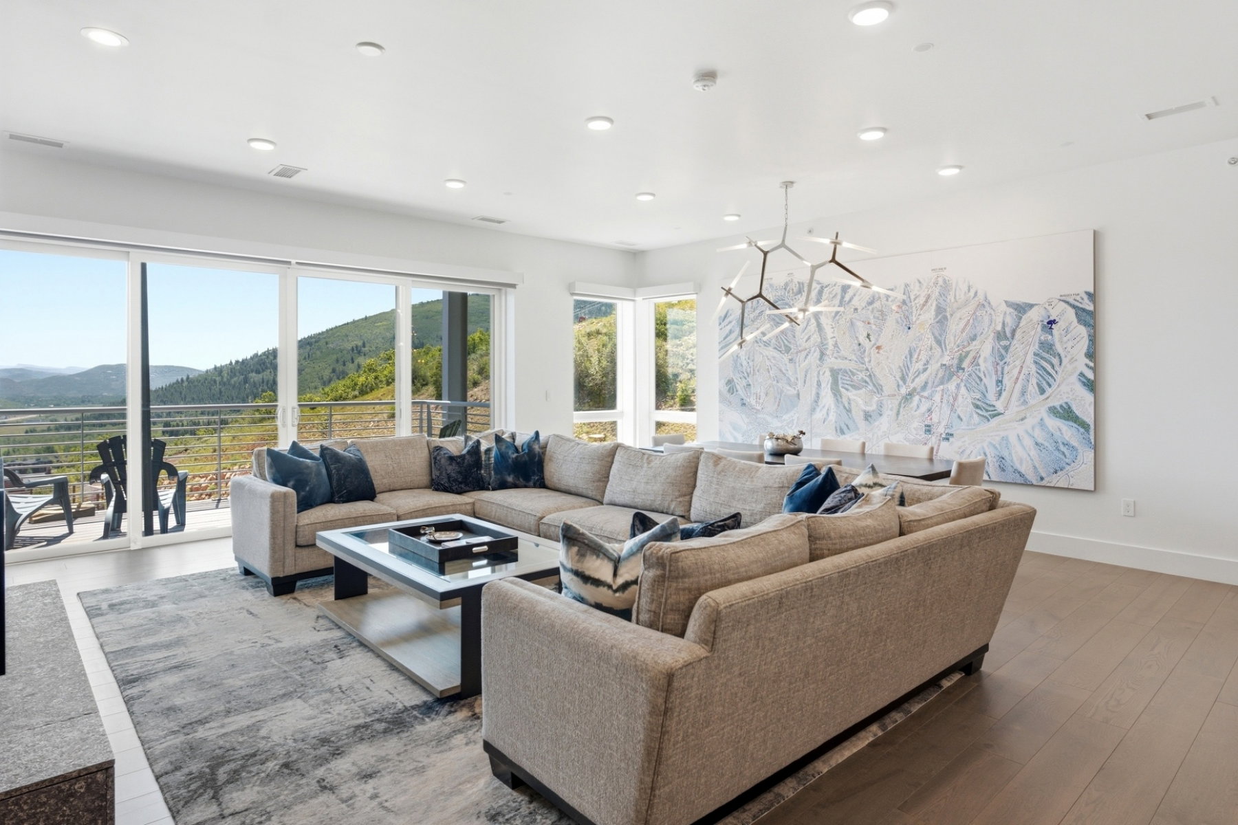 Spacious living area featuring expansive sliding glass doors, recessed lighting, wood-finish flooring, a modern chandelier, and a large artistic wall panel