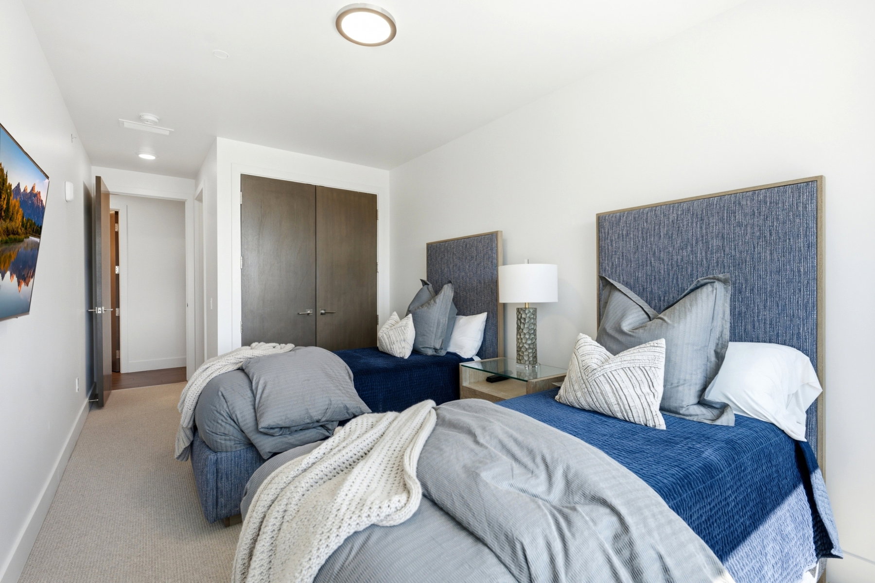 Carpeted room featuring two upholstered headboards, a wall-mounted television, and flush-mount ceiling lighting